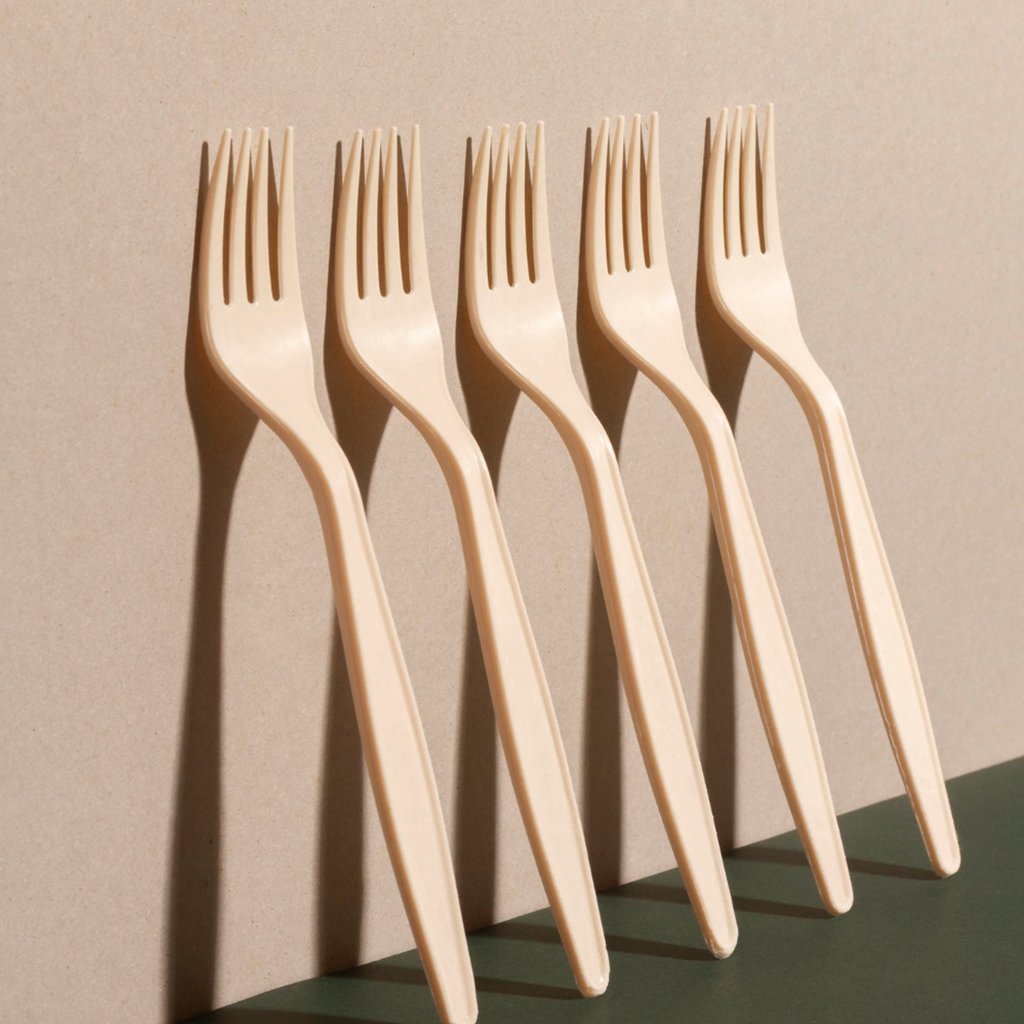 Five beige plastic forks arranged in a row with shadows cast on a beige wall