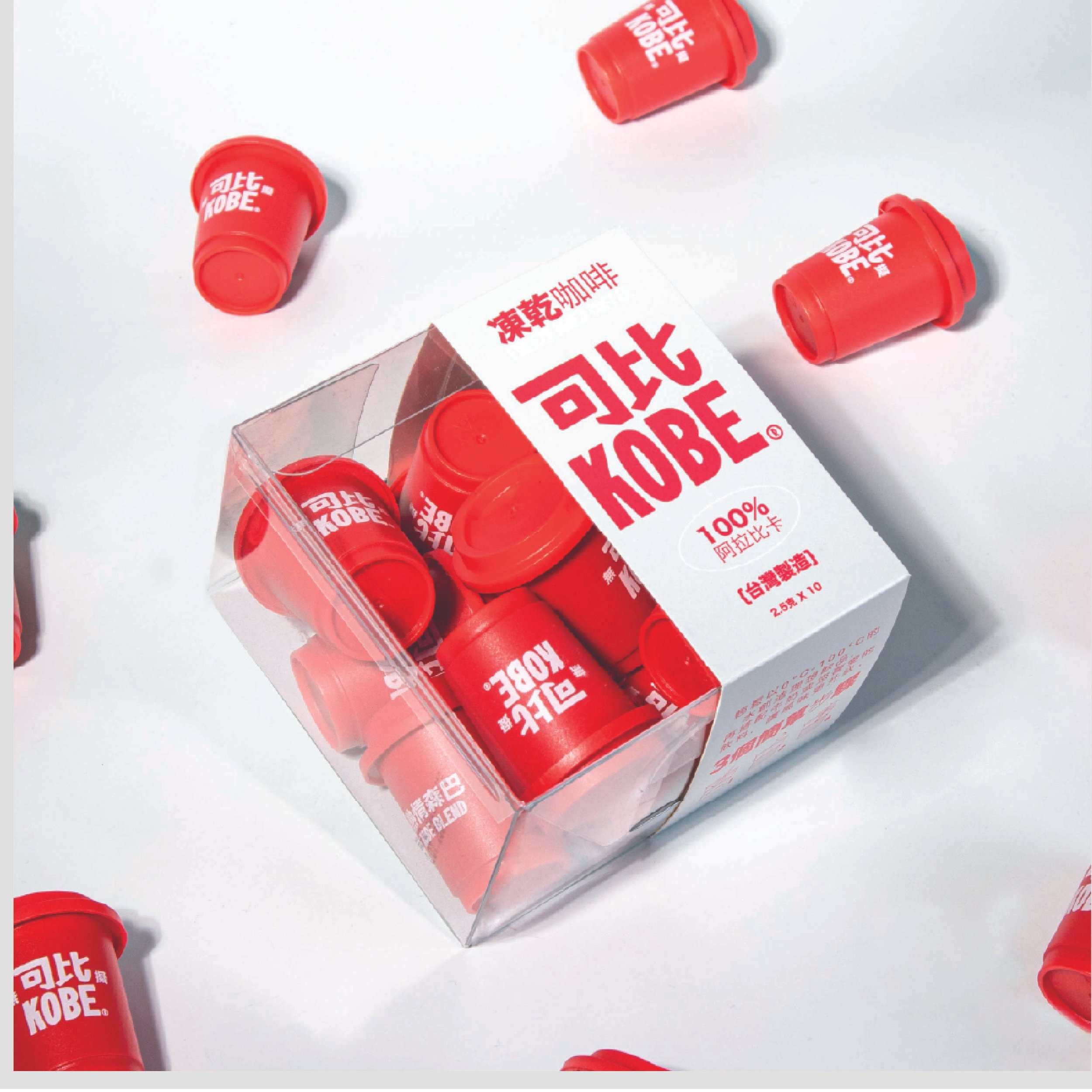 A clear plastic container filled with small red cups labeled with white and red text, with a few cups outside the container on a white surface. The cups have Asian characters and the word 'KOBE' printed on them.