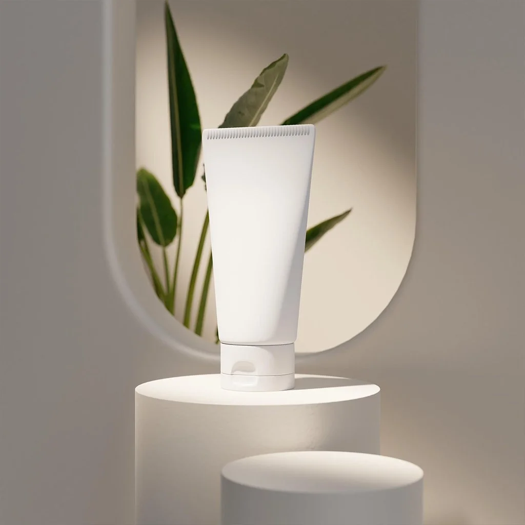 A white skincare or cosmetic tube displayed on a white cylindrical pedestal against a neutral background with a plant in a circular opening.