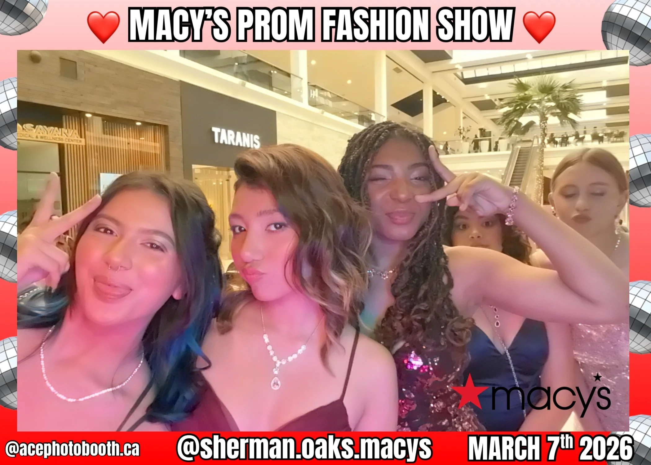 A group of young women posing together in a shopping mall during Macy's prom fashion show event on March 7th, 2026. They are making playful gestures and wearing elegant dresses and jewelry, with a Macy's sign and mall background visible.