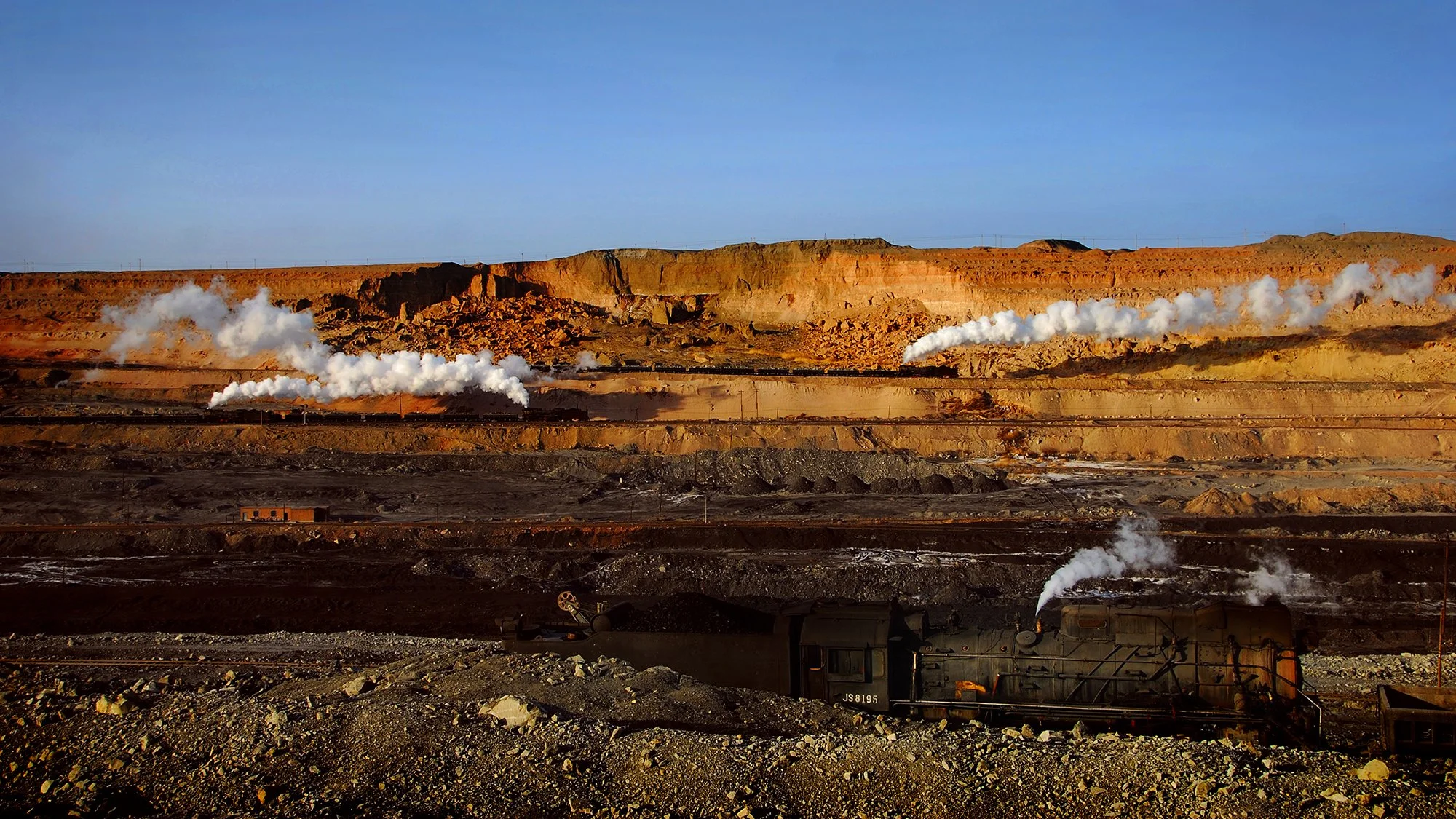  繁忙的三道嶺露天礦場。礦坑南北共有 4 台蒸汽機車在不同高度的線路上運行，2022年夏季，礦坑煤炭運輸改為汽運，鐵路停用，隨即被拆除。2010年1月。 