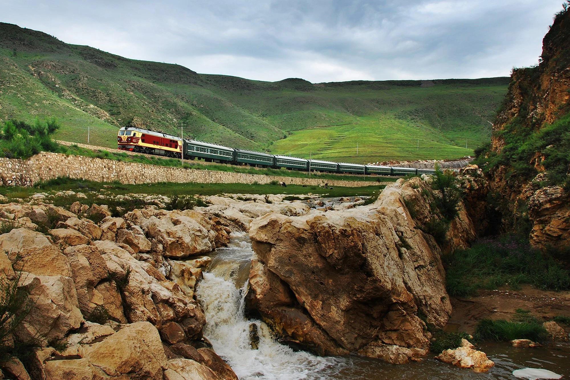  卓資山大曲線的內側，火車在這裡會減速運行。懶惰的乳牛趴在河谷中，河水在亂石間形成了小瀑布，列車悠然自得的滑過來，一幅愜意的景象。攝於2008年8月。 