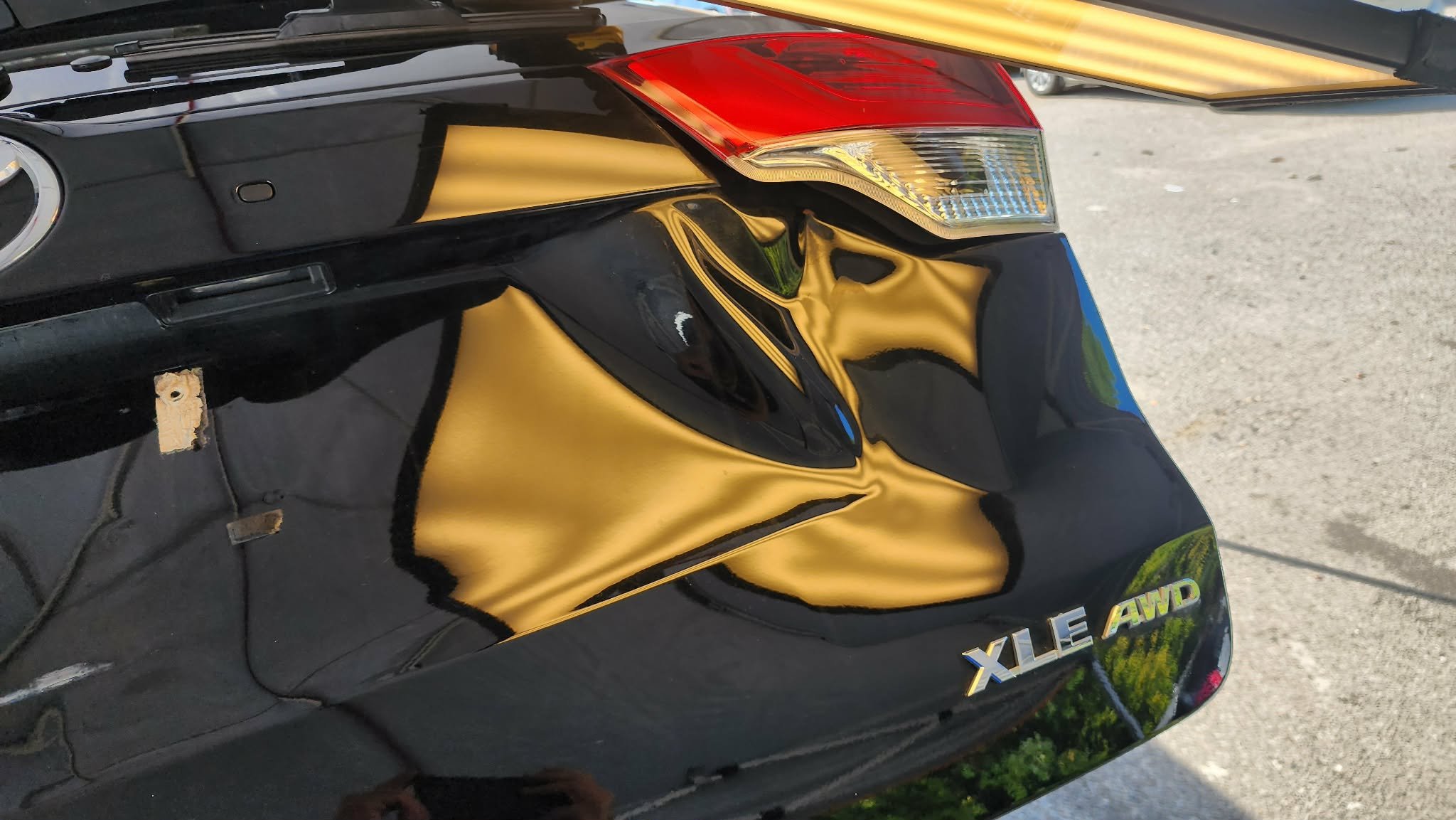 Close-up of the rear of a black car with a visible taillight and emblems that read 'XLE AWD'.