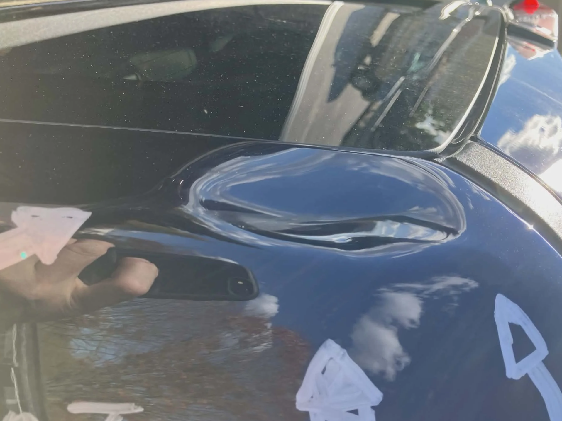 Close-up of a black car's hood with visible scratches and reflections of clouds and the sky.
