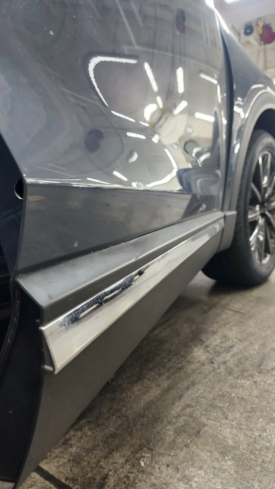 Close-up of a gray car with a dent and scratches on the side panel.