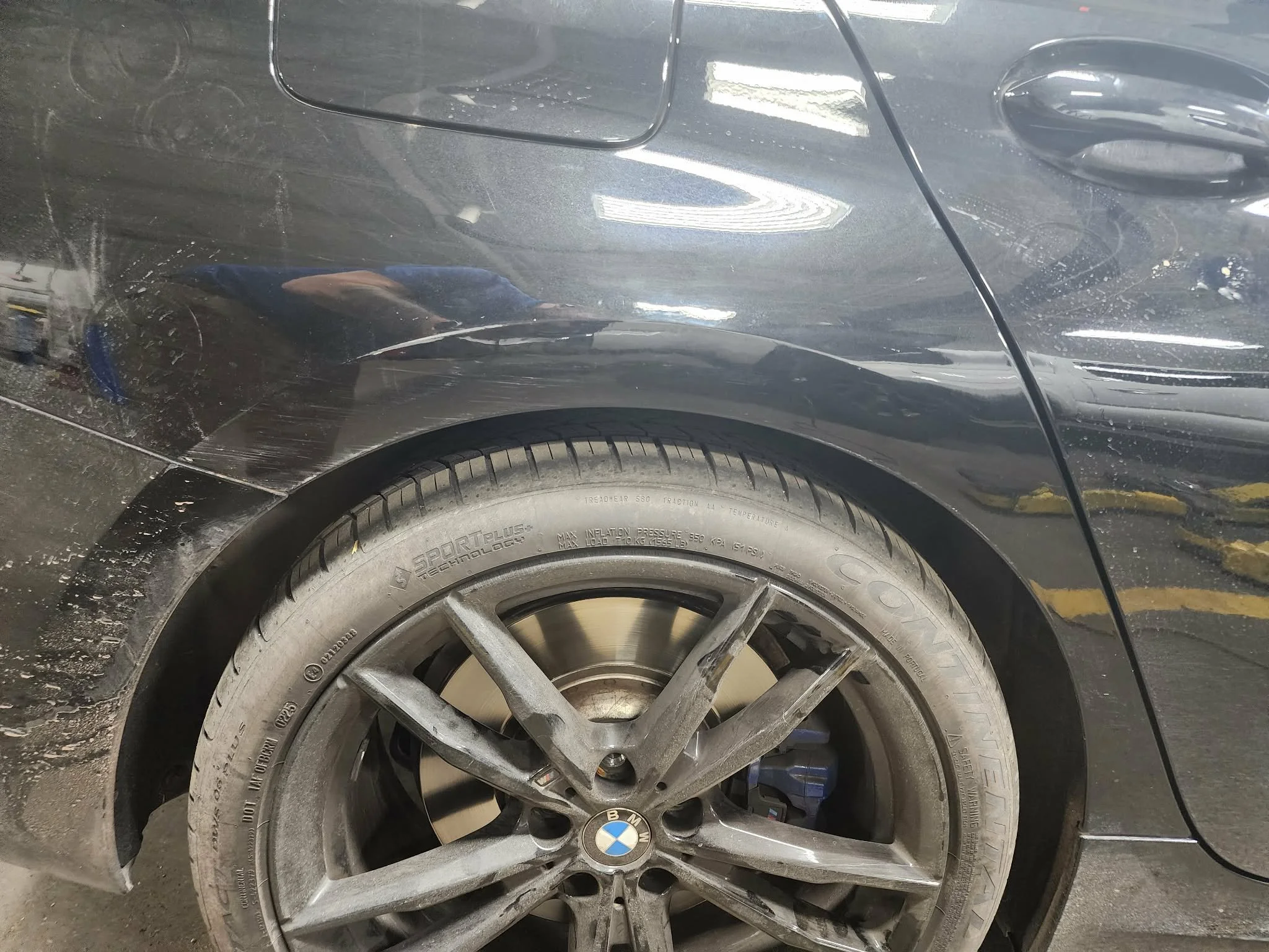 Close-up of a damaged black BMW car's rear wheel and fender, with visible scratches and dirt.
