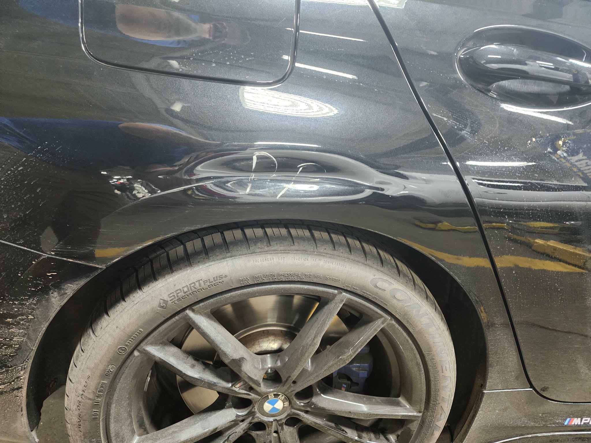 Black BMW car with damage to the rear left side panel above the wheel, which has a large dent and scratches.