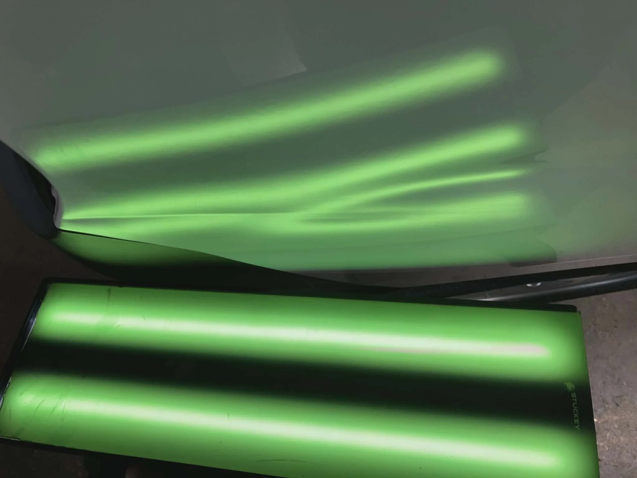 Close-up of green neon lights reflecting on a smooth surface, creating glowing streaks of light.