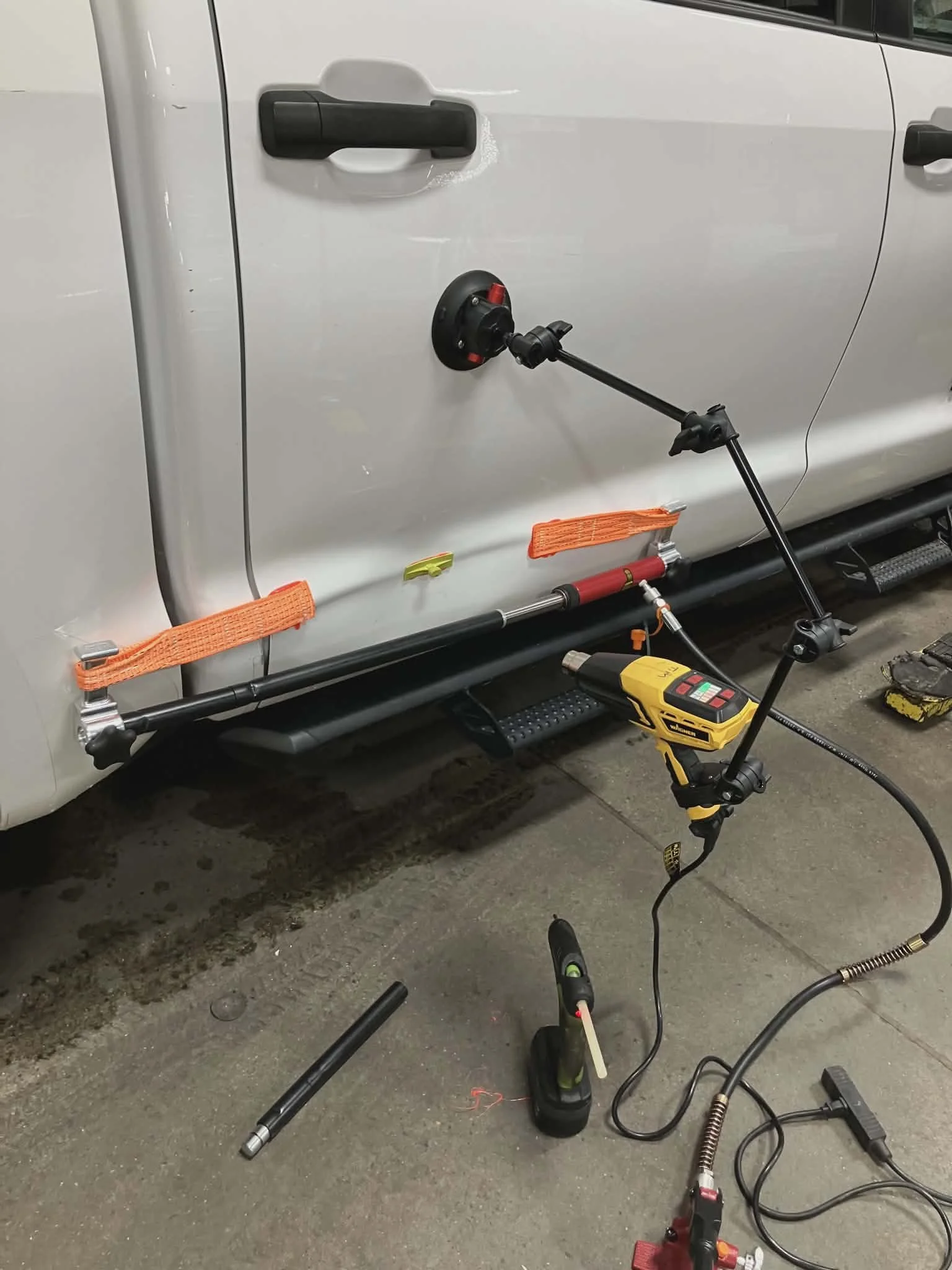Photo of a white vehicle with load suspension or alignment setup tools attached to the side, including a yellow power tool, a black control device, and orange straps.