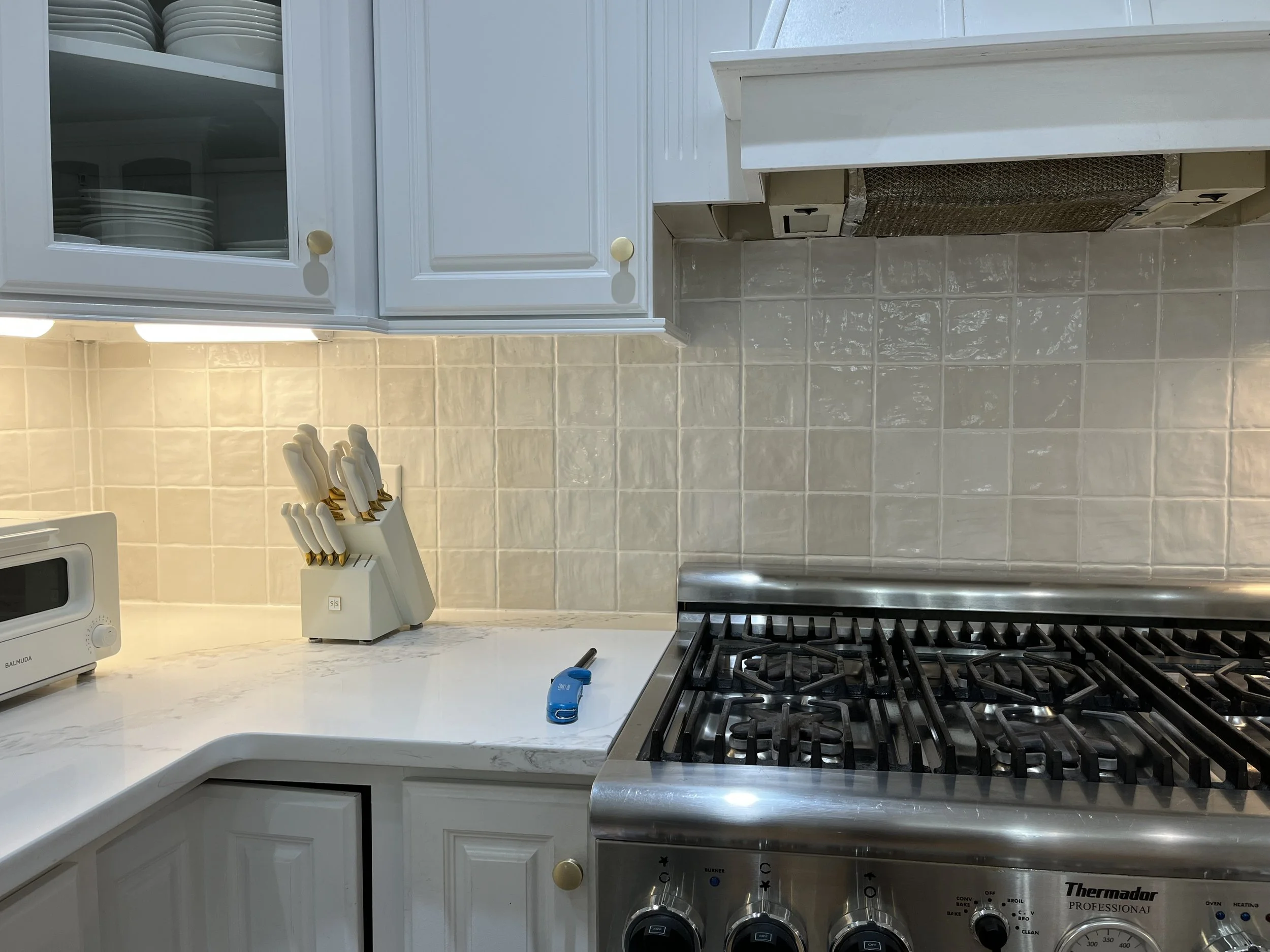 Kitchen with white cabinets, beige backsplash tiles, a microwave, a knife block, a blue lighter, and a stainless steel Thermador gas stove.