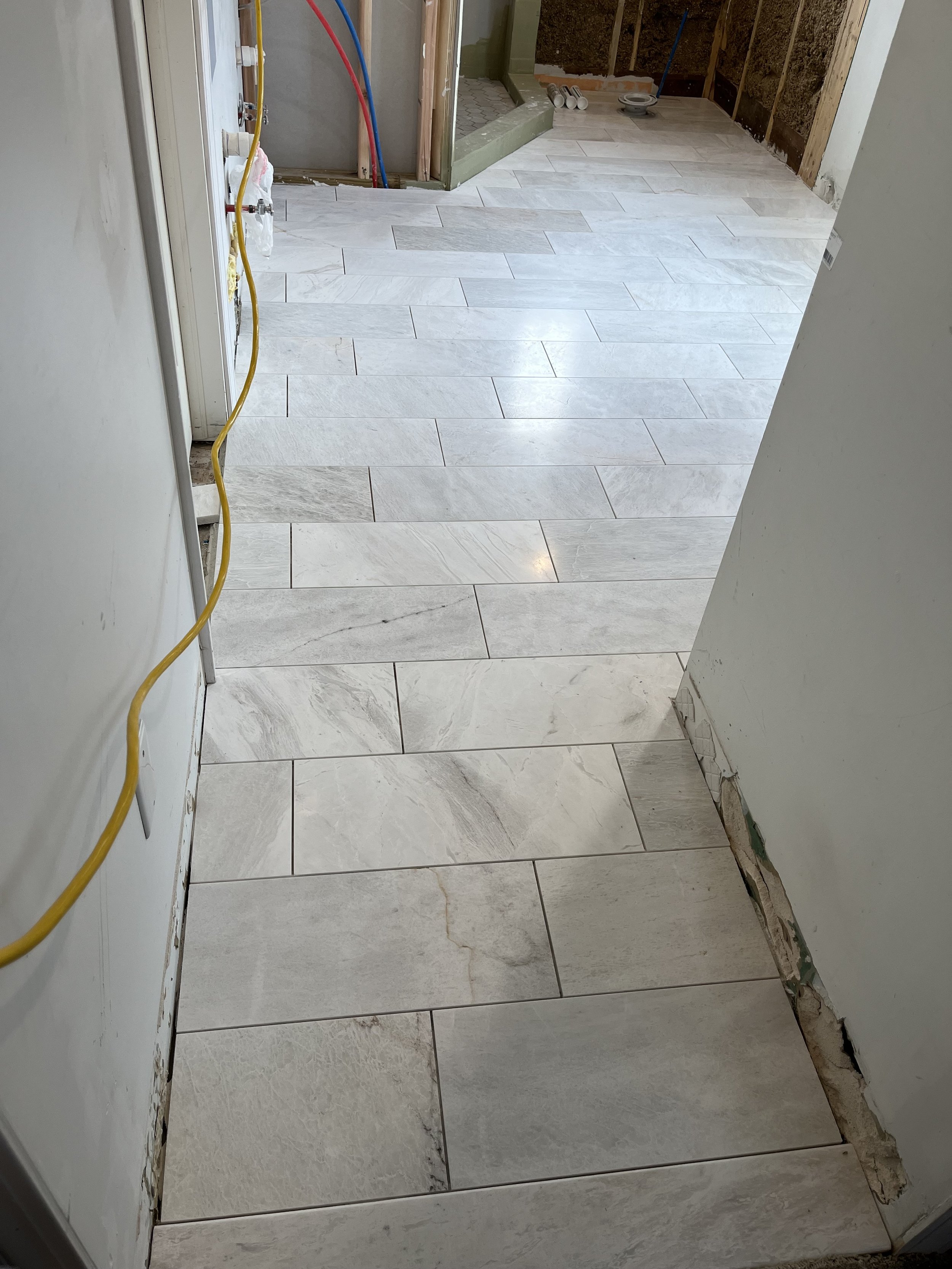 Construction area with a newly installed tiled floor, exposed pipes, and unfinished wall sections.