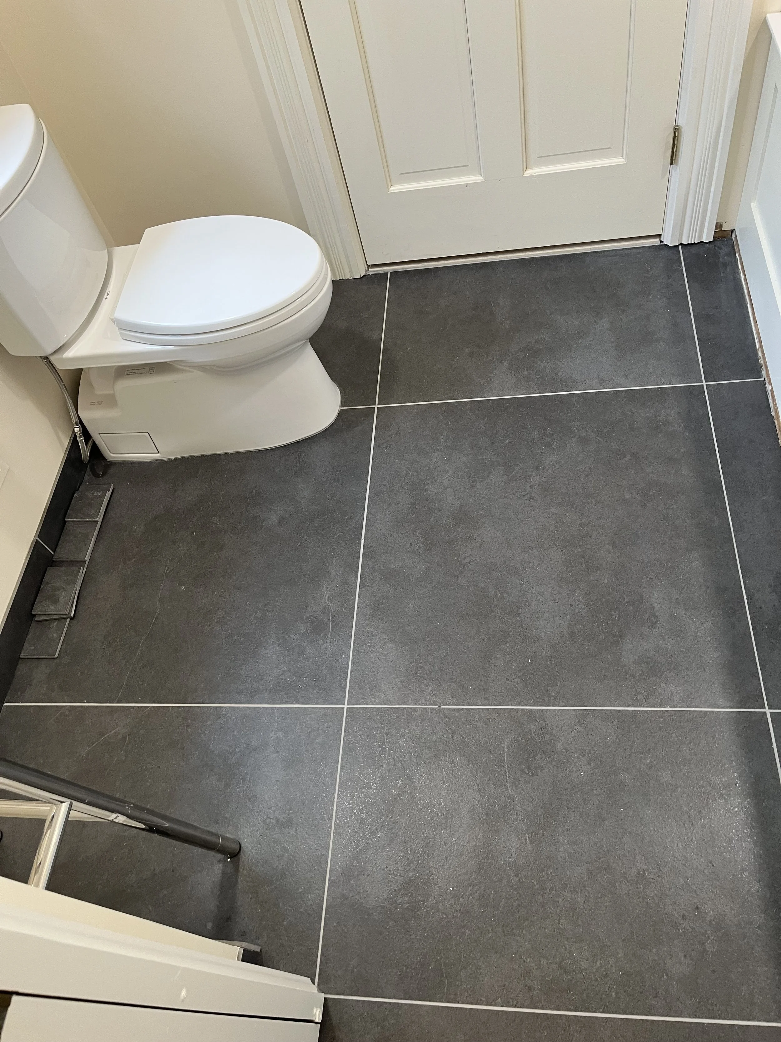 Bathroom with dark gray tiled floor, white toilet, and closed door.