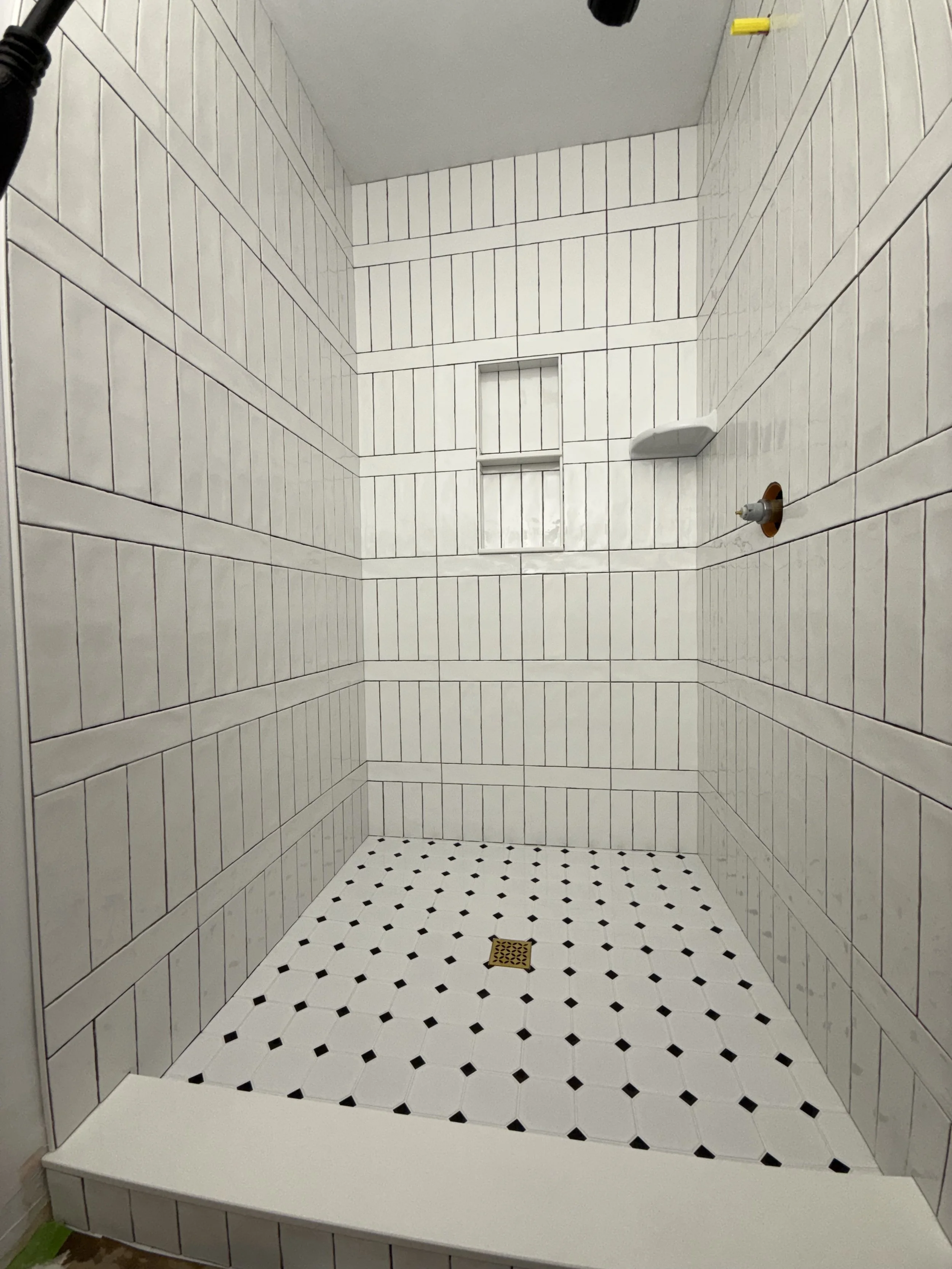 Empty shower with tiled walls and floor, including a drain in the center, and no fixtures installed yet.