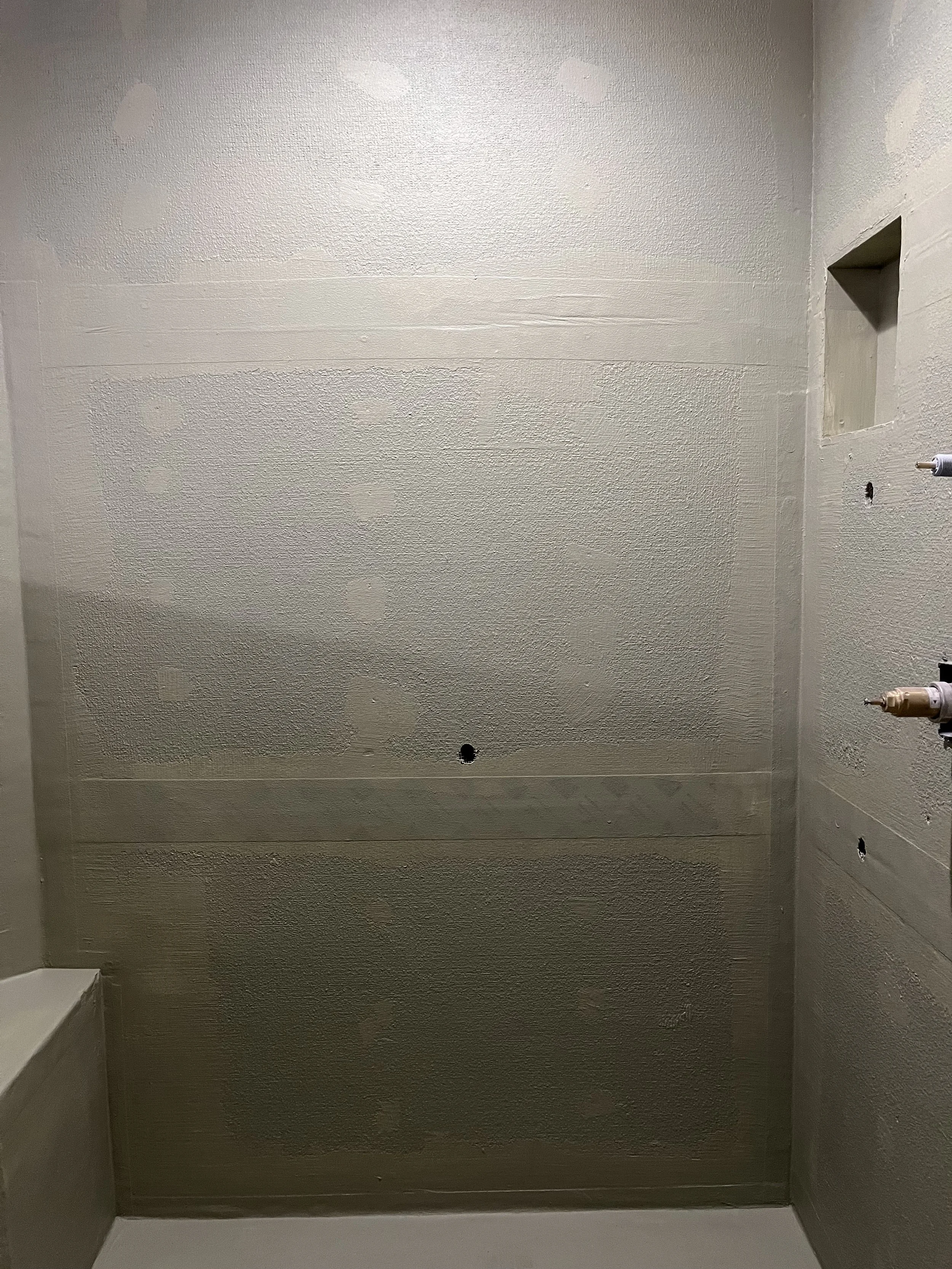 Unfinished drywall wall with holes and patchwork, partially textured, in a room under construction.