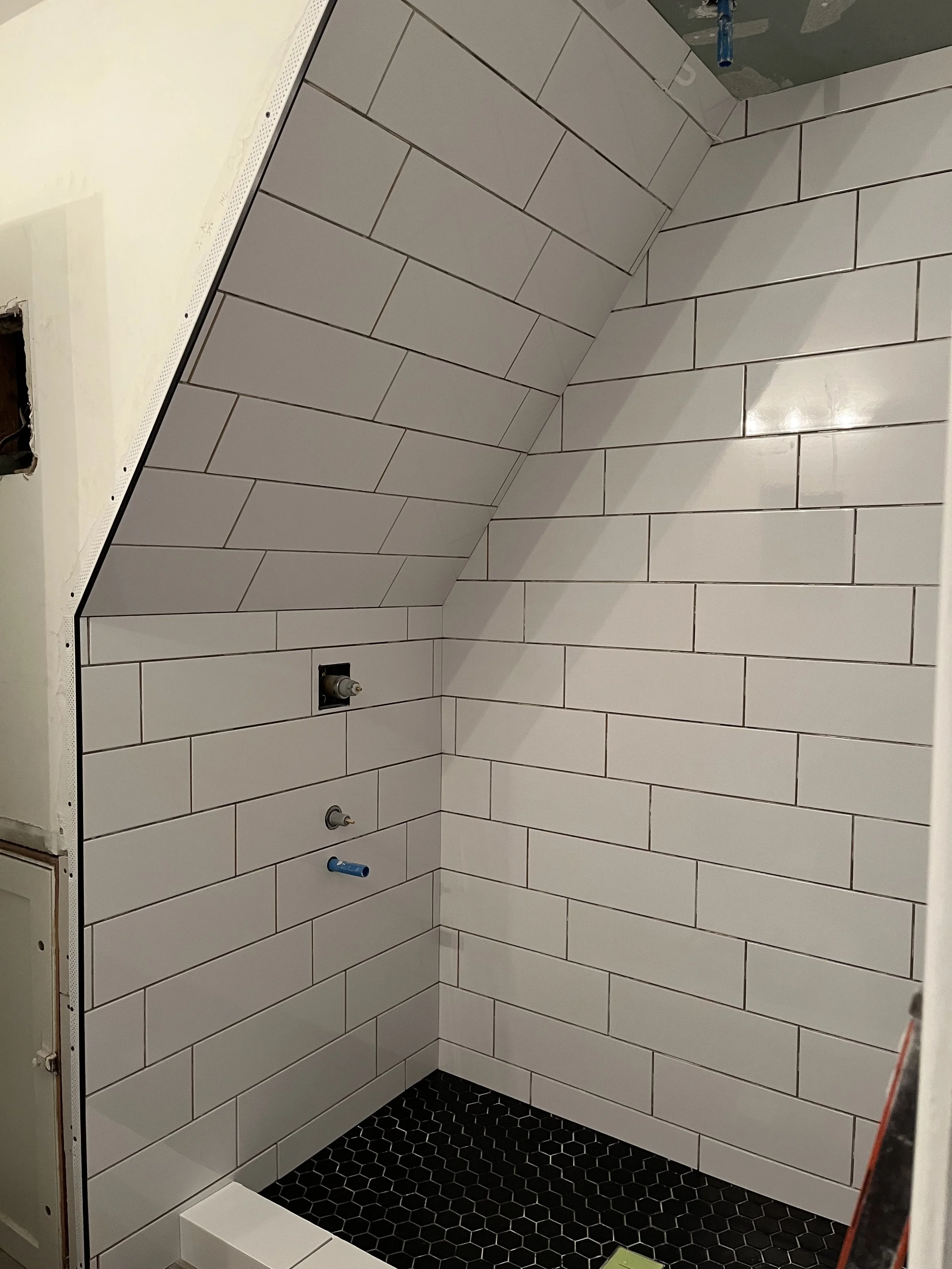 Under construction bathroom with tiled walls and black hexagon floor tiles, plumbing fixtures not installed yet.
