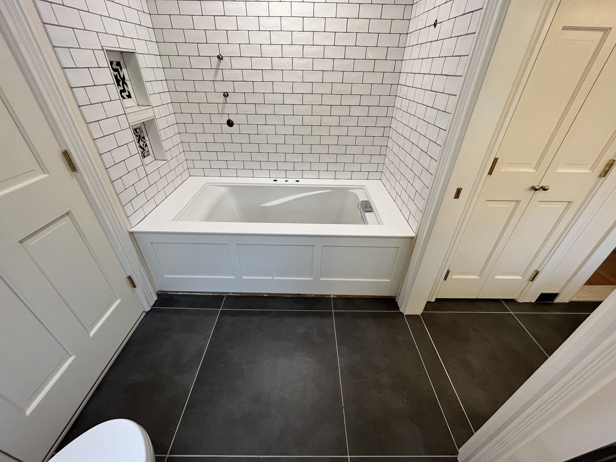 Bathroom with white tiled walls, a bathtub, built-in shelves, and dark floor tiles.