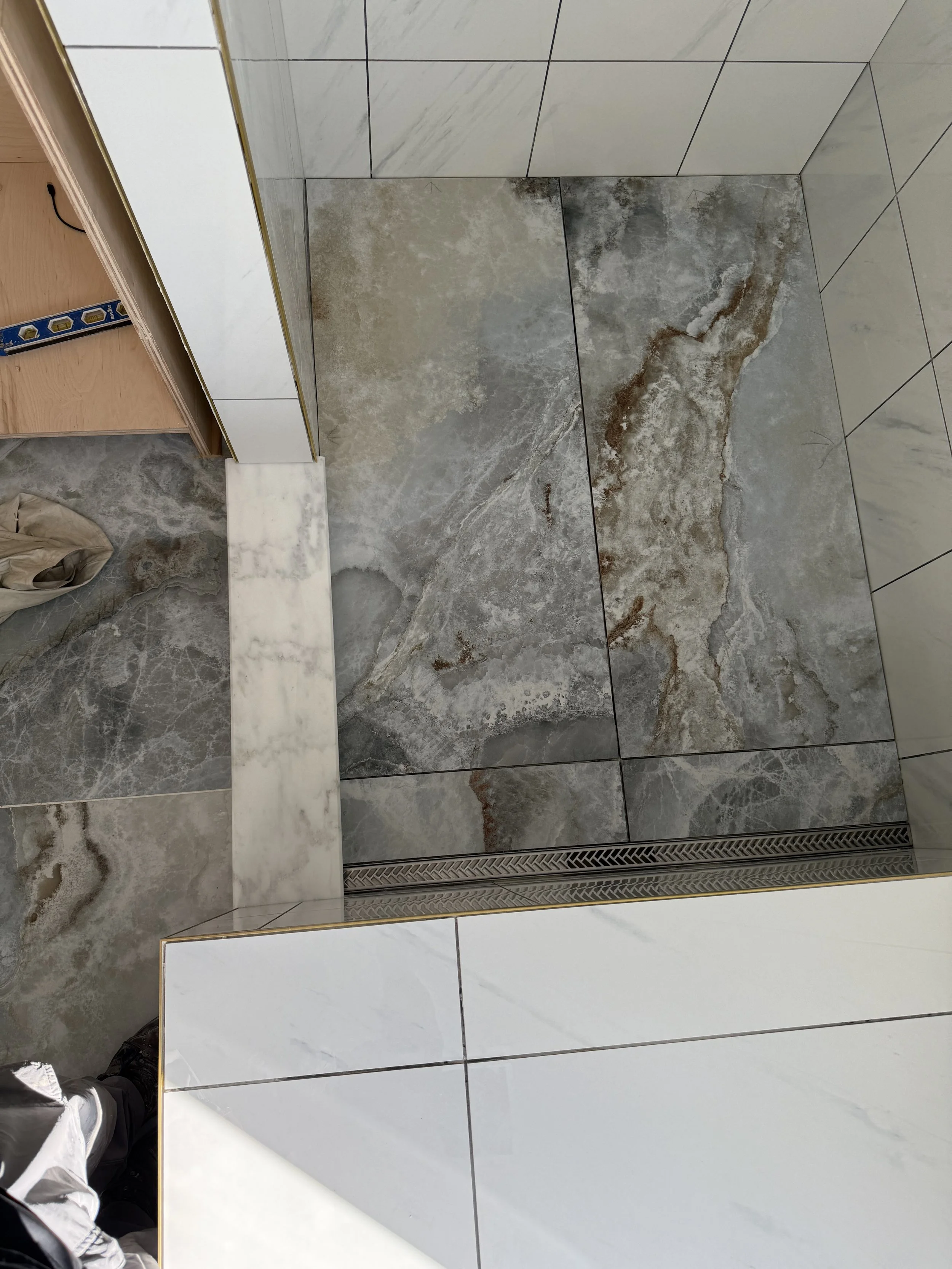 Close-up view of a tiled floor with marble and stone tiles, featuring a linear drain at the edge.