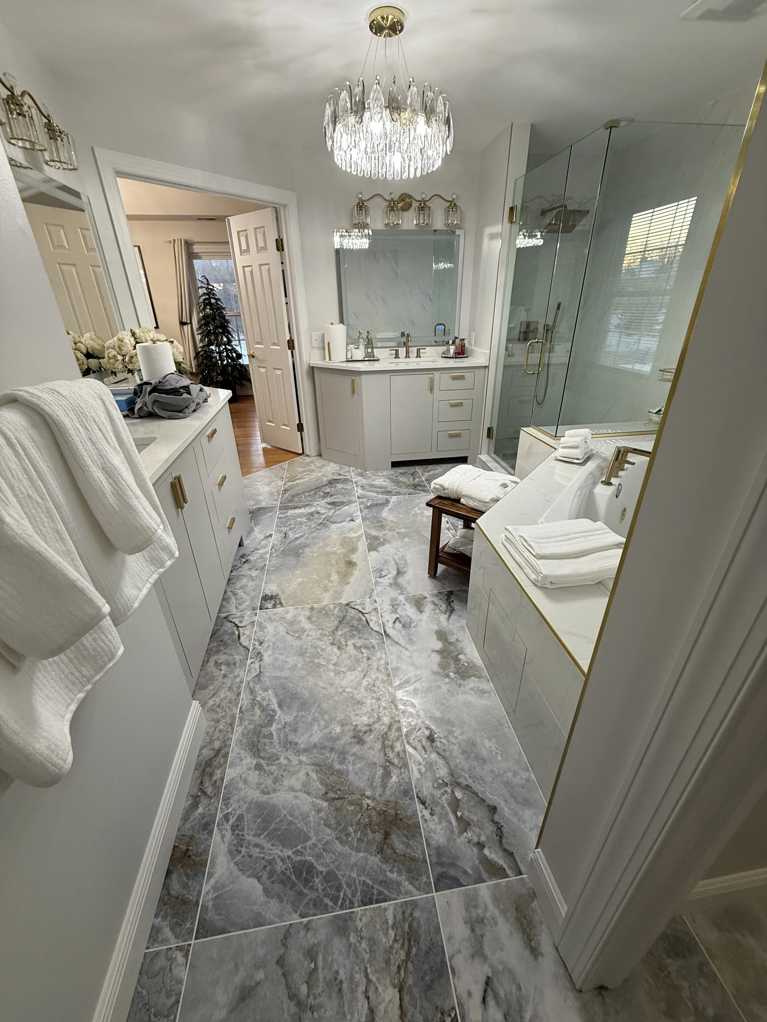 Luxury bathroom with marble flooring, white cabinets, a glass shower, and elegant lighting fixtures.