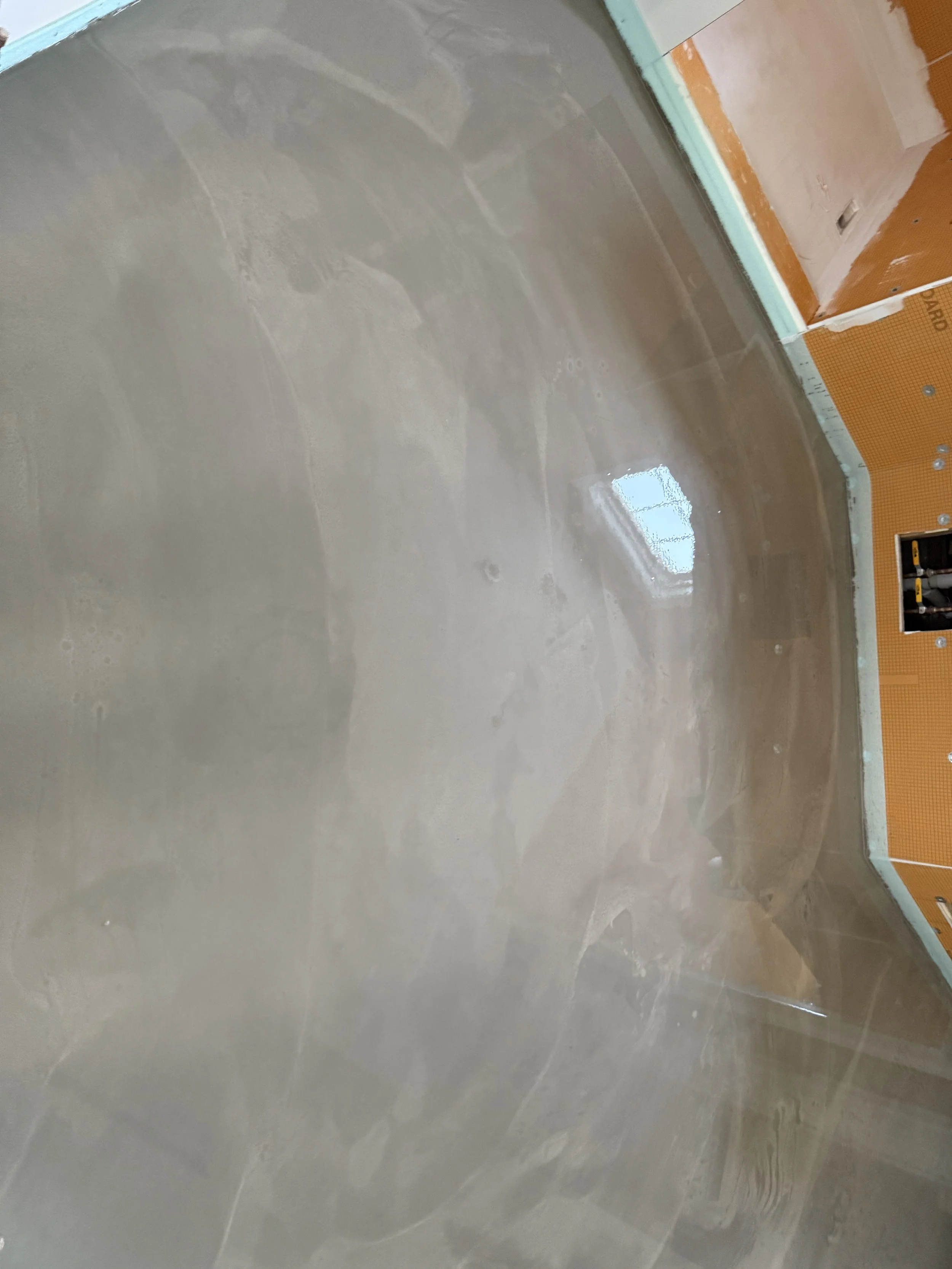 Interior of a room under construction with a freshly poured concrete floor and partially finished walls, with some wall electrical outlets visible.