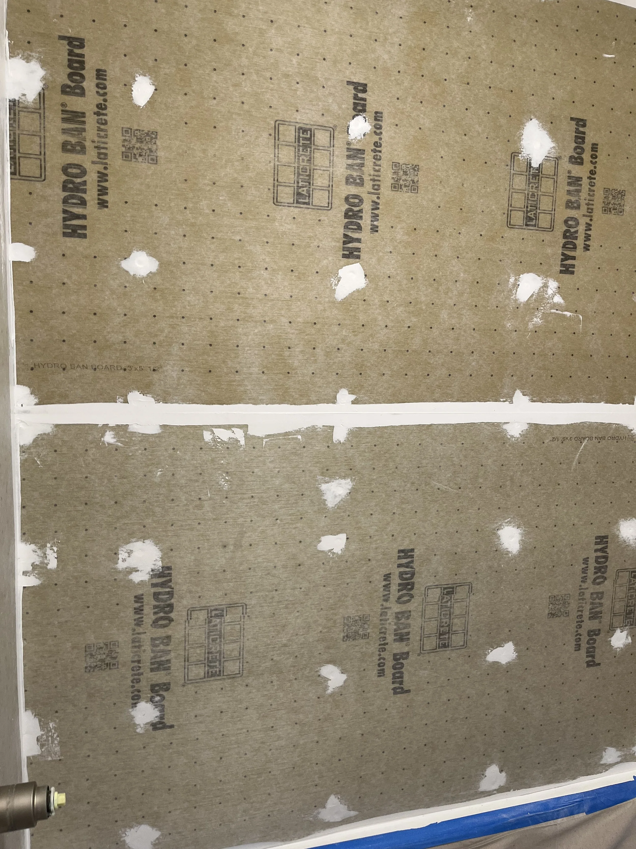 Two large pieces of brown drywall with black text and logos, fastened to a wall, with a white joint compound line along the middle, and a metallic object visible in the bottom left corner.