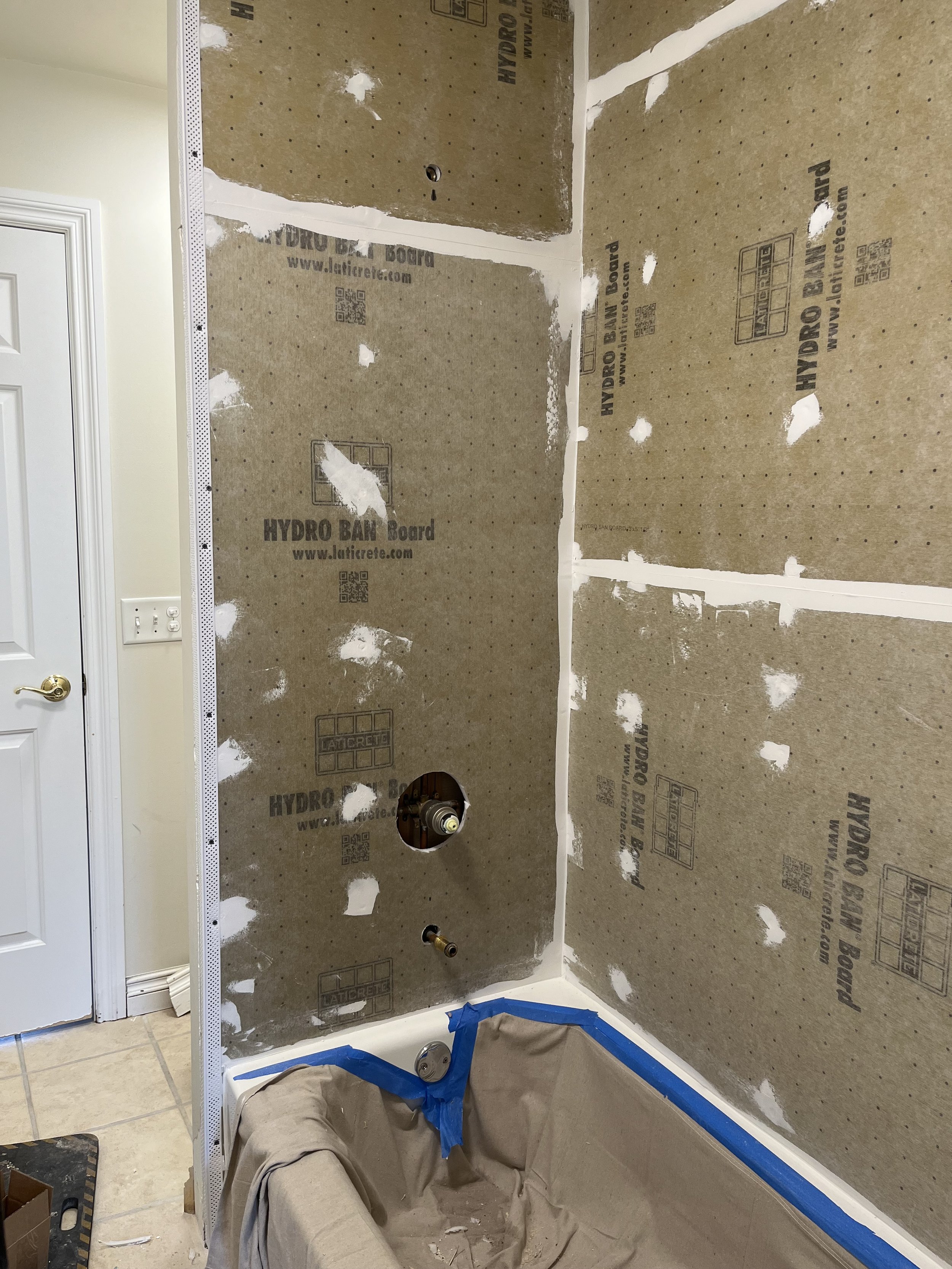 Bathroom renovation in progress, with drywall installed around the bathtub area, taped and mudded seams visible, and plumbing fixtures exposed.