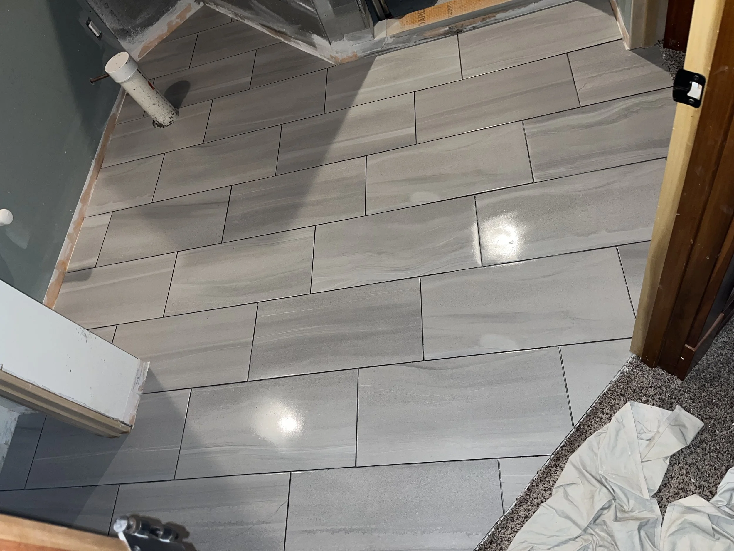 Newly installed light gray marble floor tiles in a room under renovation, with construction tools and materials visible.