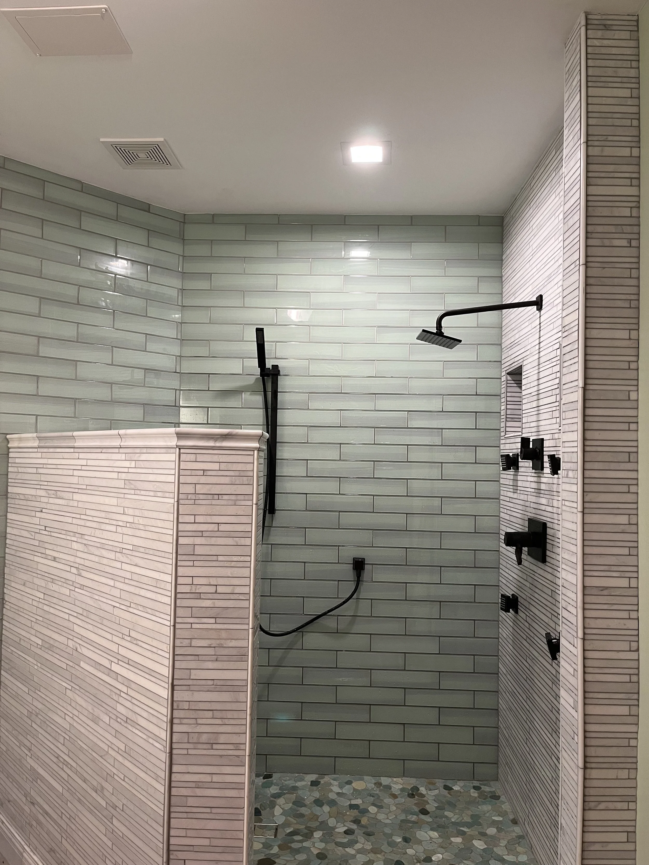 Modern shower area with green subway tiles, pebble floor, and black shower fixtures.