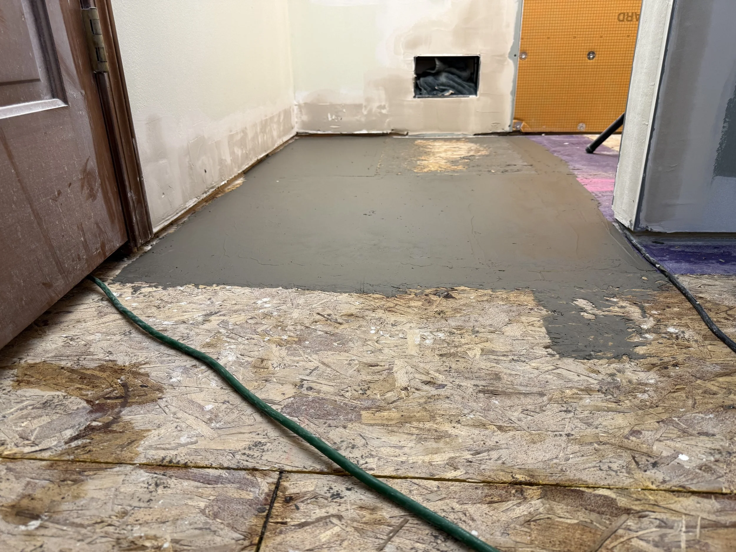 A partially renovated room with a newly poured concrete floor, exposed drywall, and construction materials. Cables are visible on the floor.