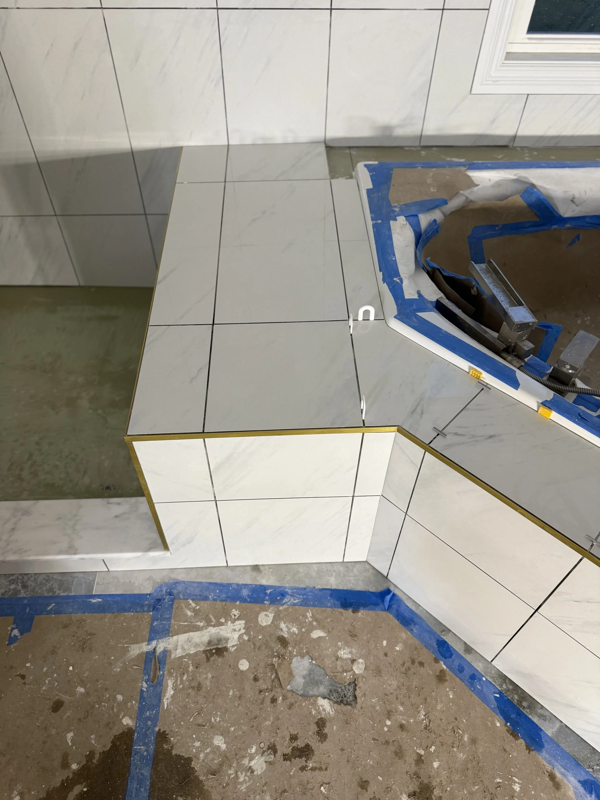 Bathroom under construction with tiled walls and a partially installed countertop. Blue painter's tape around the edges of the counter, with a plastic sink basin inset.