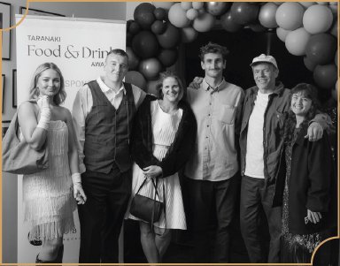 Six people standing together at a social event, in front of a balloon arch and a sign that says "Food & Drink".