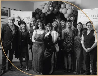 Group of people standing together at an indoor event, with a decorated backdrop featuring balloons in black and pink tones.