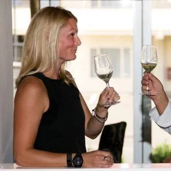 Woman with blonde hair holding a glass of white wine at a social gathering.