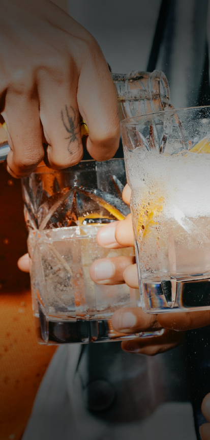 People clinking glasses with ice, lemon slices, and clear beverages in a celebratory toast.