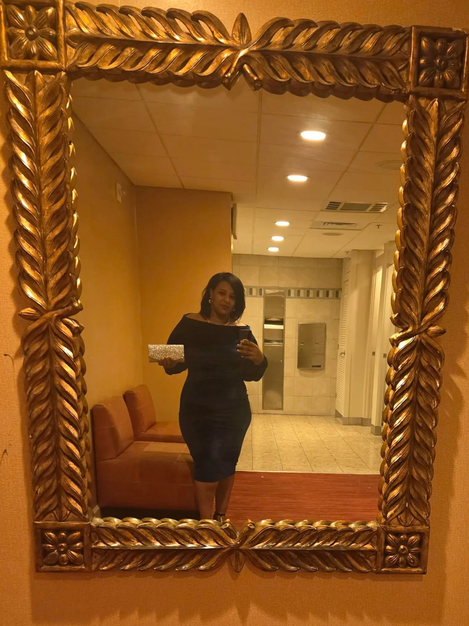 Gracefully Unfiltered author Tracey Joseph in a navy blue dress holding a glittery clutch taking a mirror selfie in a hotel lobby