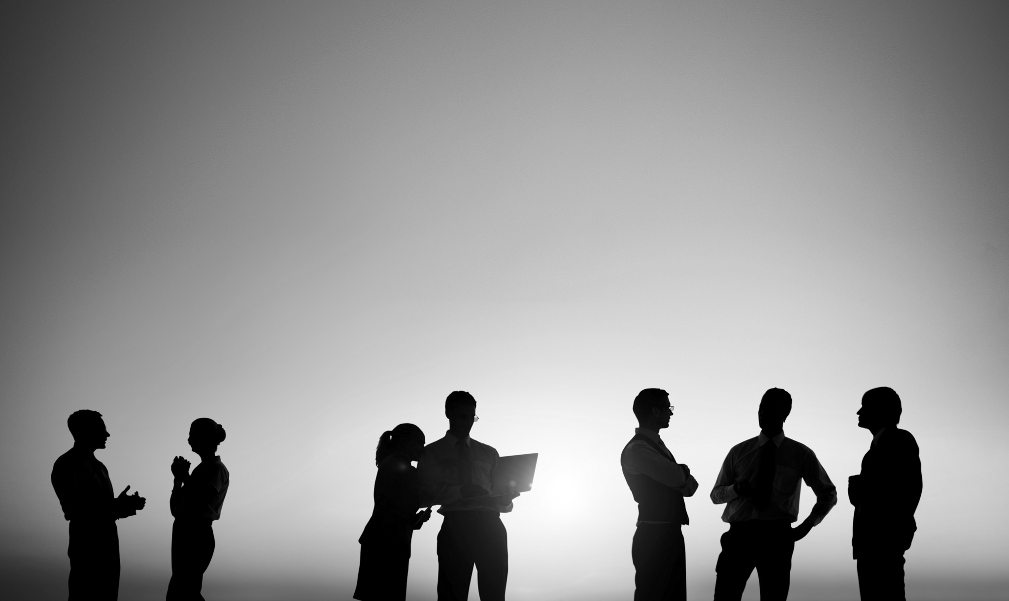 Silhouettes of nine people engaging in conversation and working outdoors during sunset or sunrise.