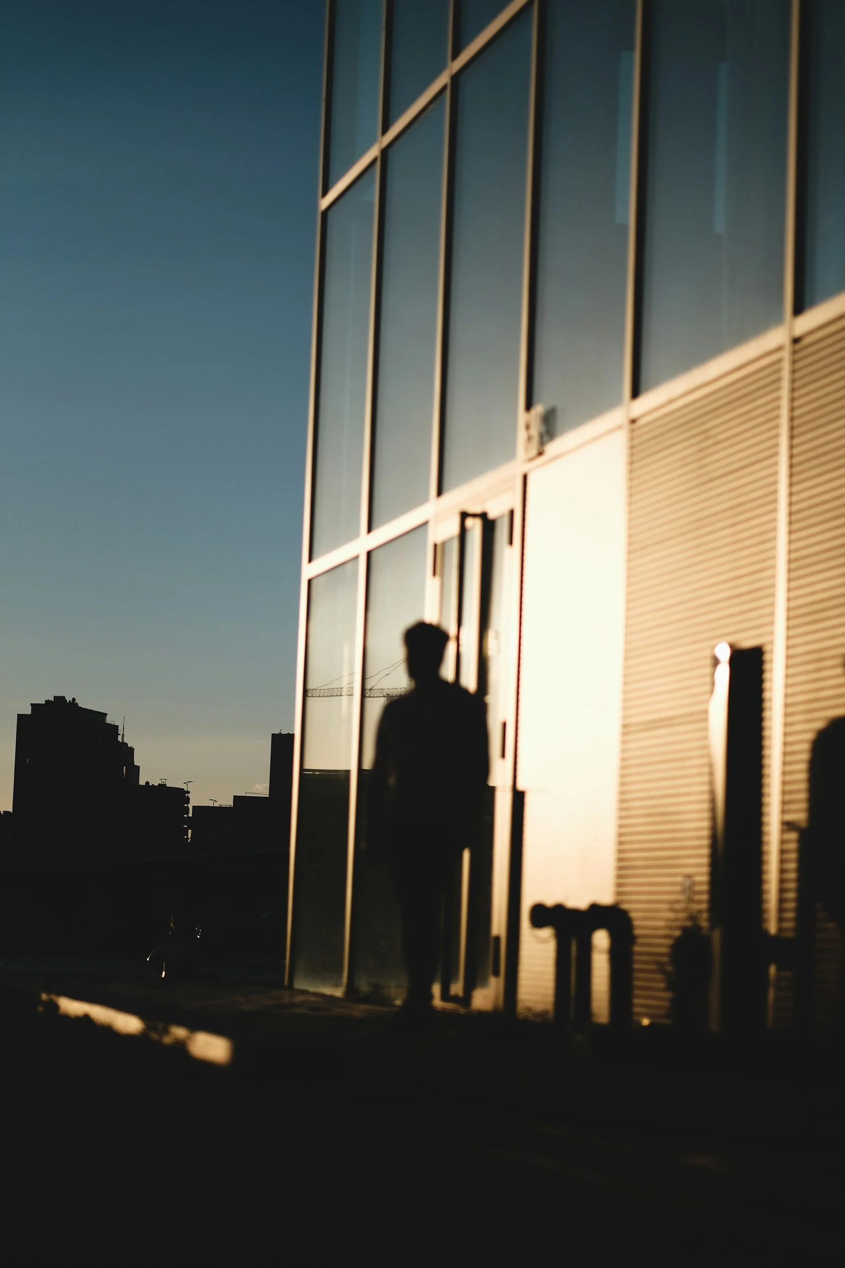 Silhouette of a person standing outside a modern glass building during sunset or sunrise.