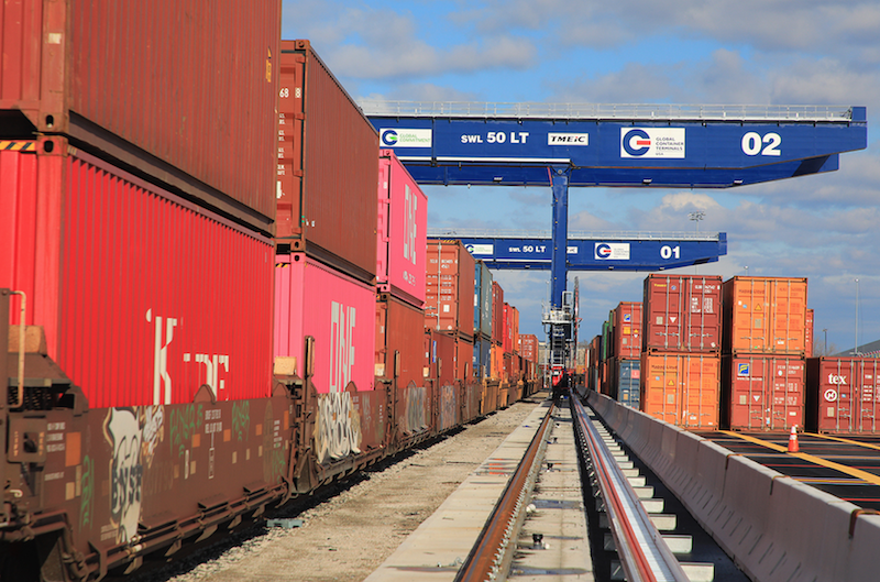 View of a container shipping yard with stacked cargo containers and large cranes used for loading and unloading containers.