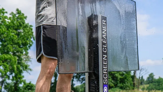 Person rinsing a large outdoor screen cleaner on a screen in a park.