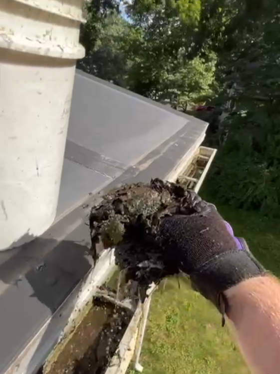 Person wearing a glove cleaning debris from a roof gutter.