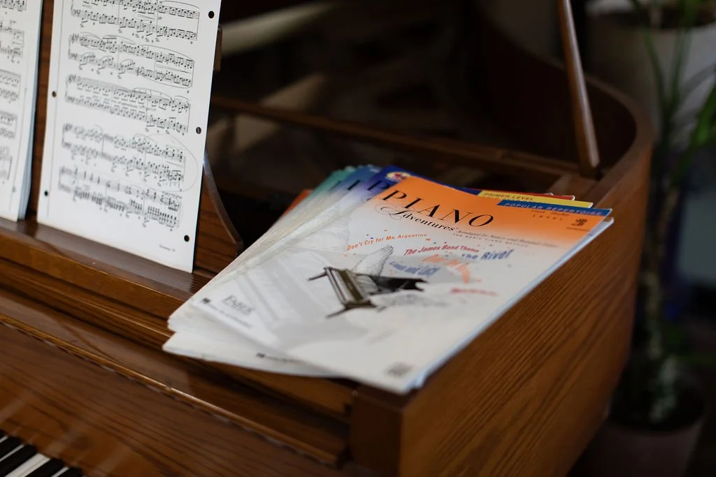 A wooden piano with sheet music on a stand and some magazines about pianos.