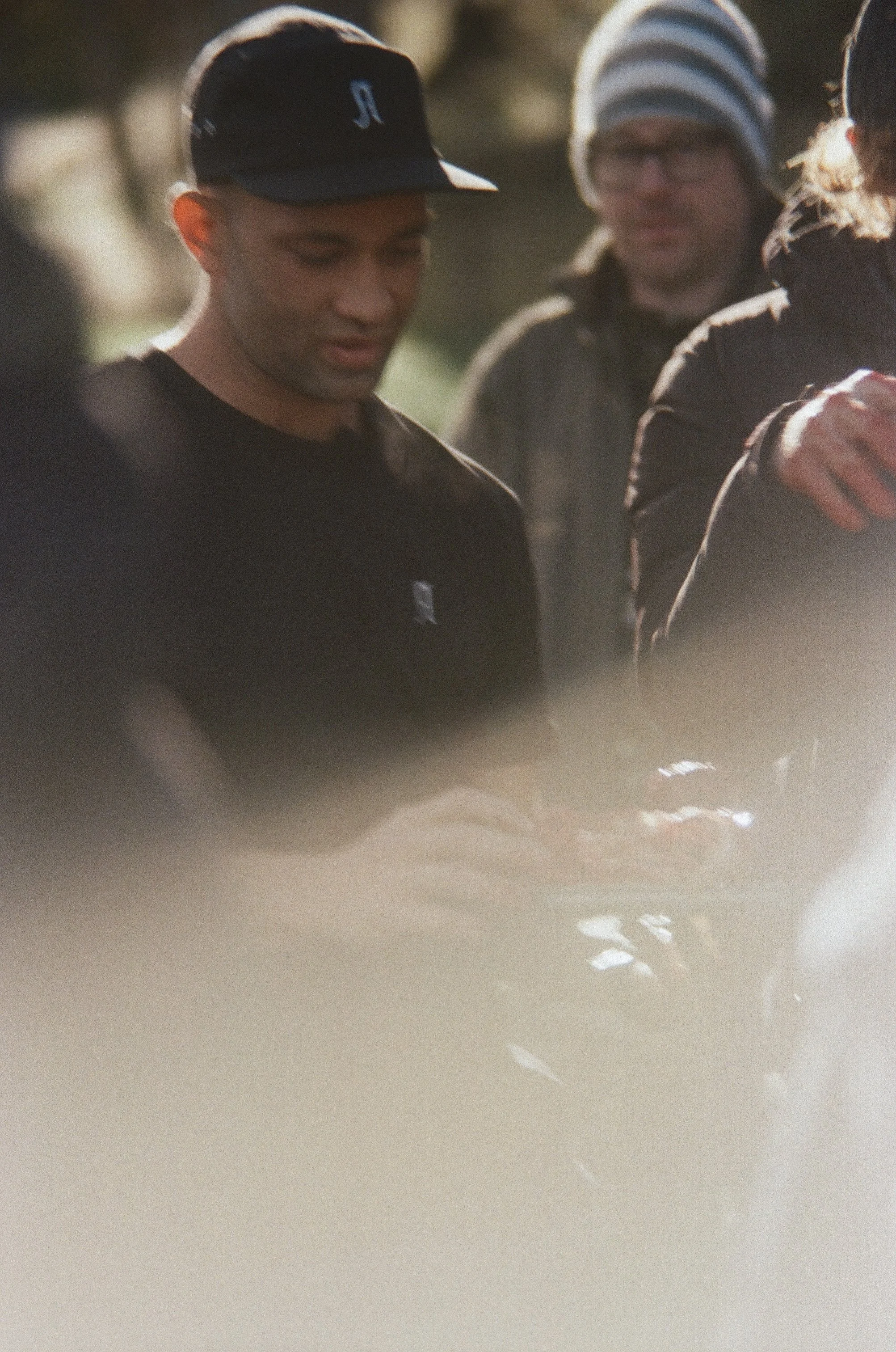 People standing outdoors, some wearing hats and jackets, appear to be engaged in an activity or conversation.