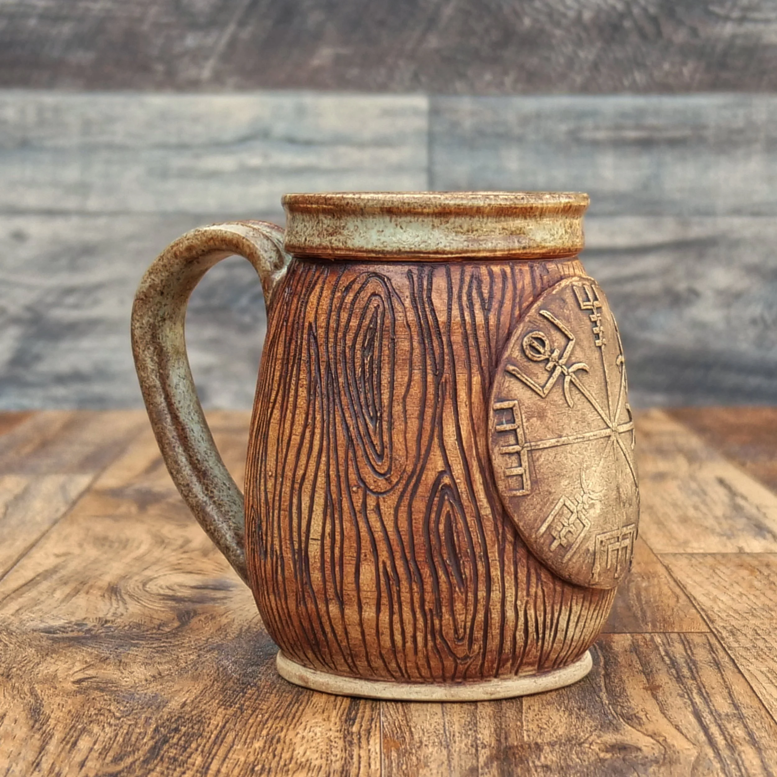 Handmade stoneware Wayfinder Mug by Elderkiln Ceramics featuring a raised Vegvísir symbol, hand-carved woodgrain texture, and warm earth-tone glazes.