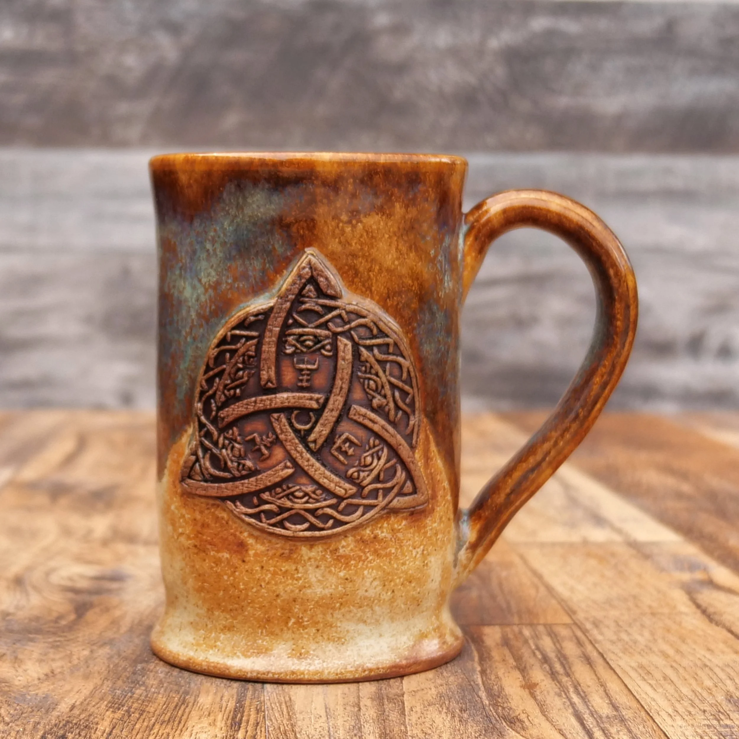 Handmade Trinity Knot Mug by Elderkiln Ceramics featuring a sculpted Celtic knot design and layered earthy brown and mineral-toned stoneware glazes.