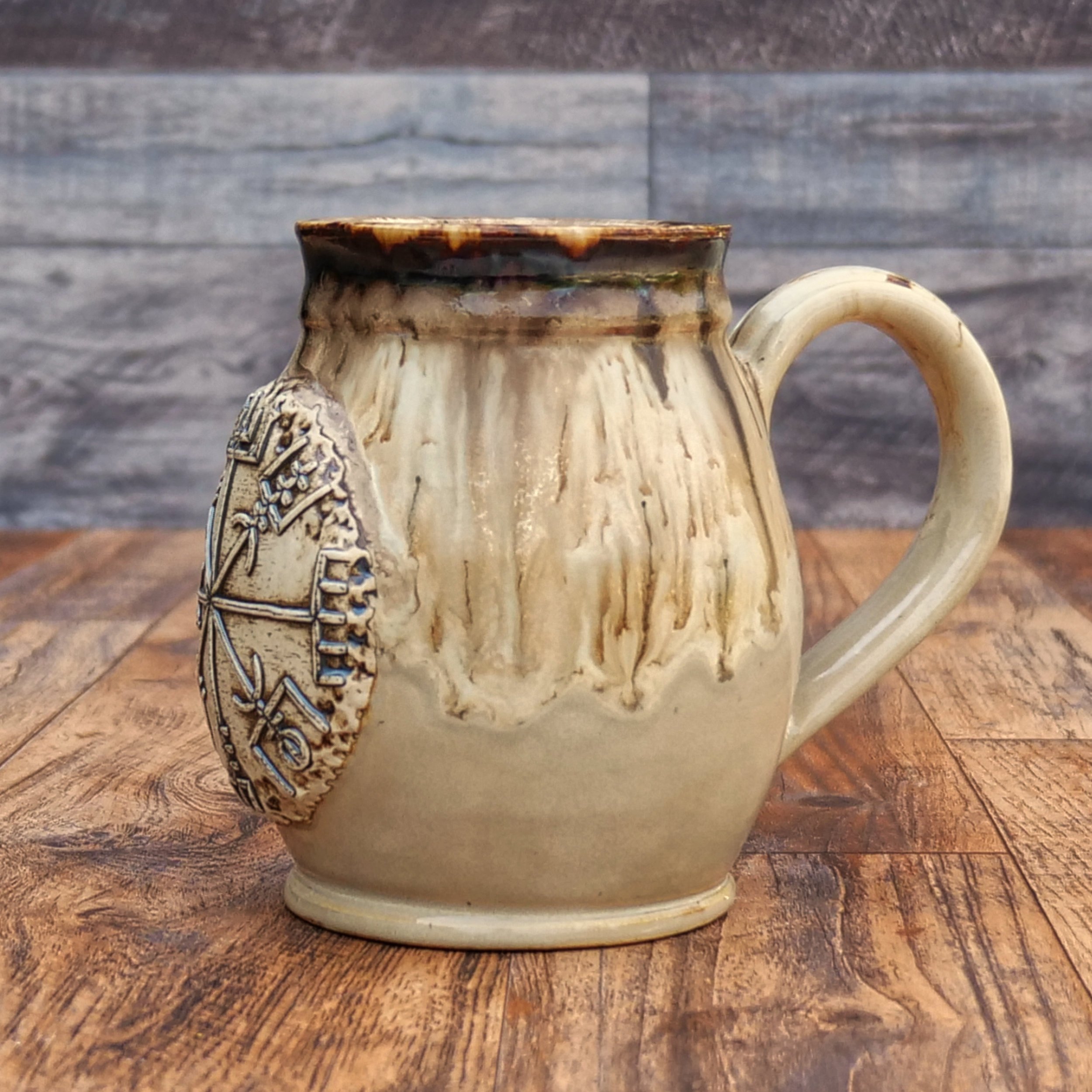 Handmade Wayfinder Mug by Elderkiln Ceramics featuring a sculpted Vegvísir symbol and layered earthy stoneware glazes in cream, amber, and brown tones.