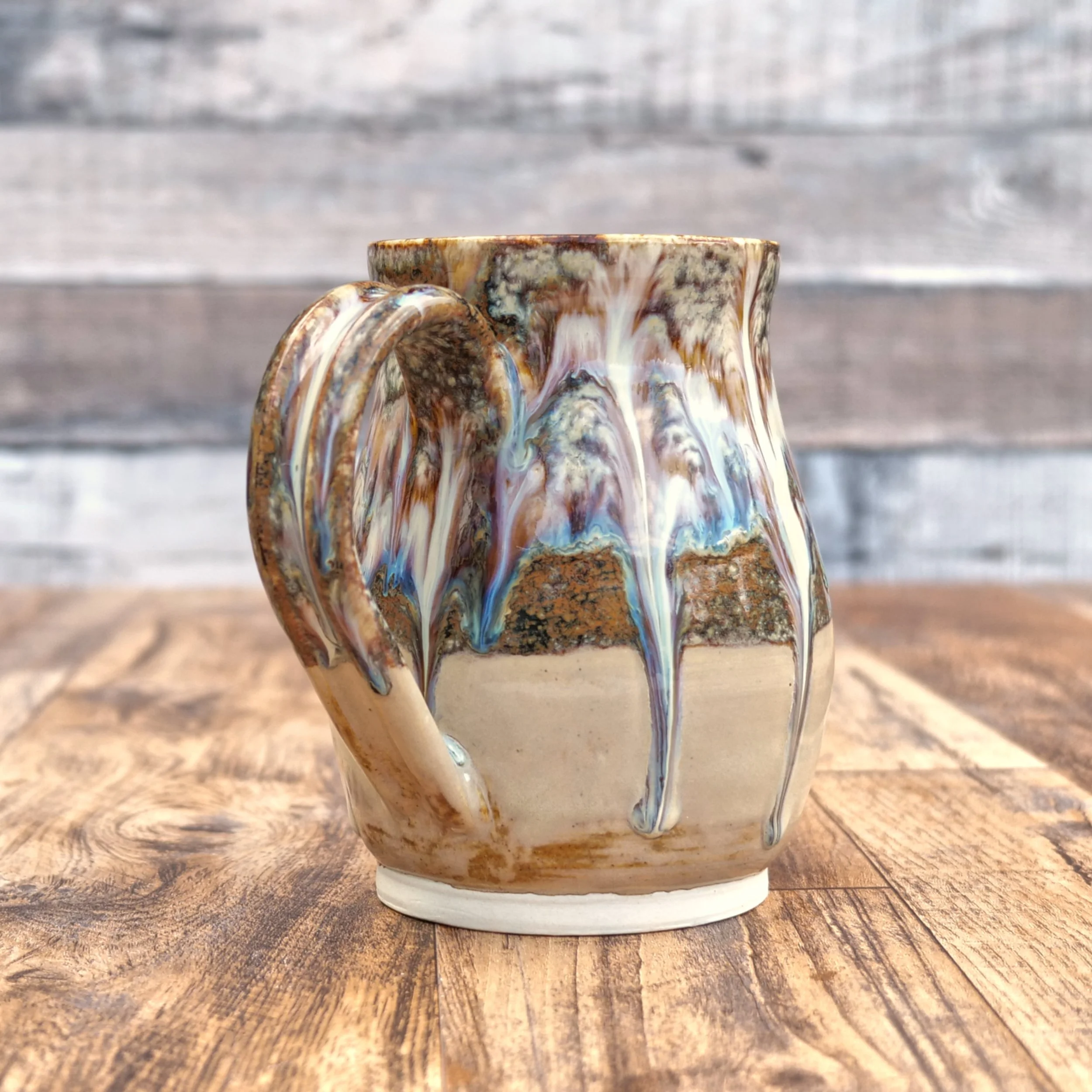 Handmade stoneware Cascade Mug by Elderkiln Ceramics featuring flowing layered glazes in earthy brown, cream, and mineral tones on a rustic pottery mug.