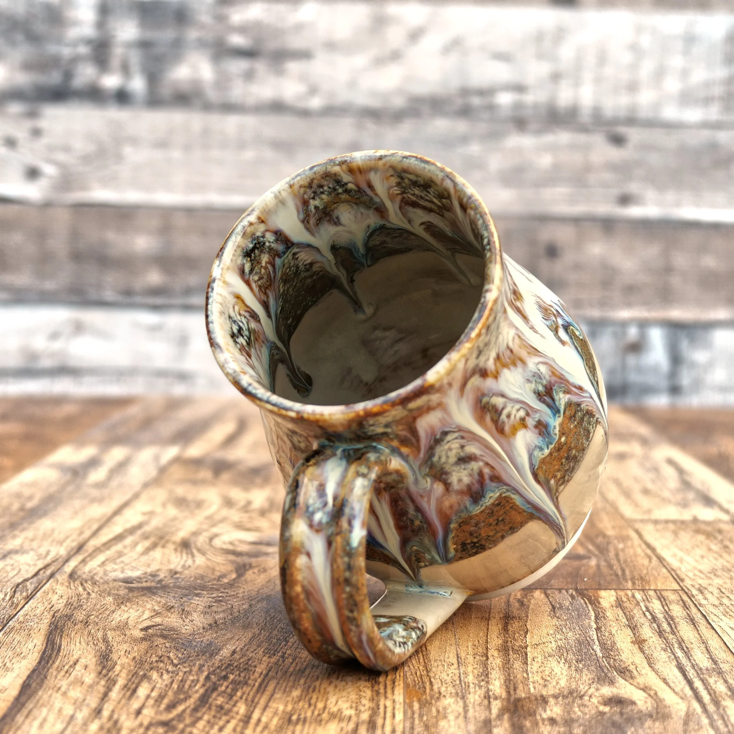 Handmade stoneware Cascade Mug by Elderkiln Ceramics featuring flowing layered glazes in earthy brown, cream, and mineral tones on a rustic pottery mug.