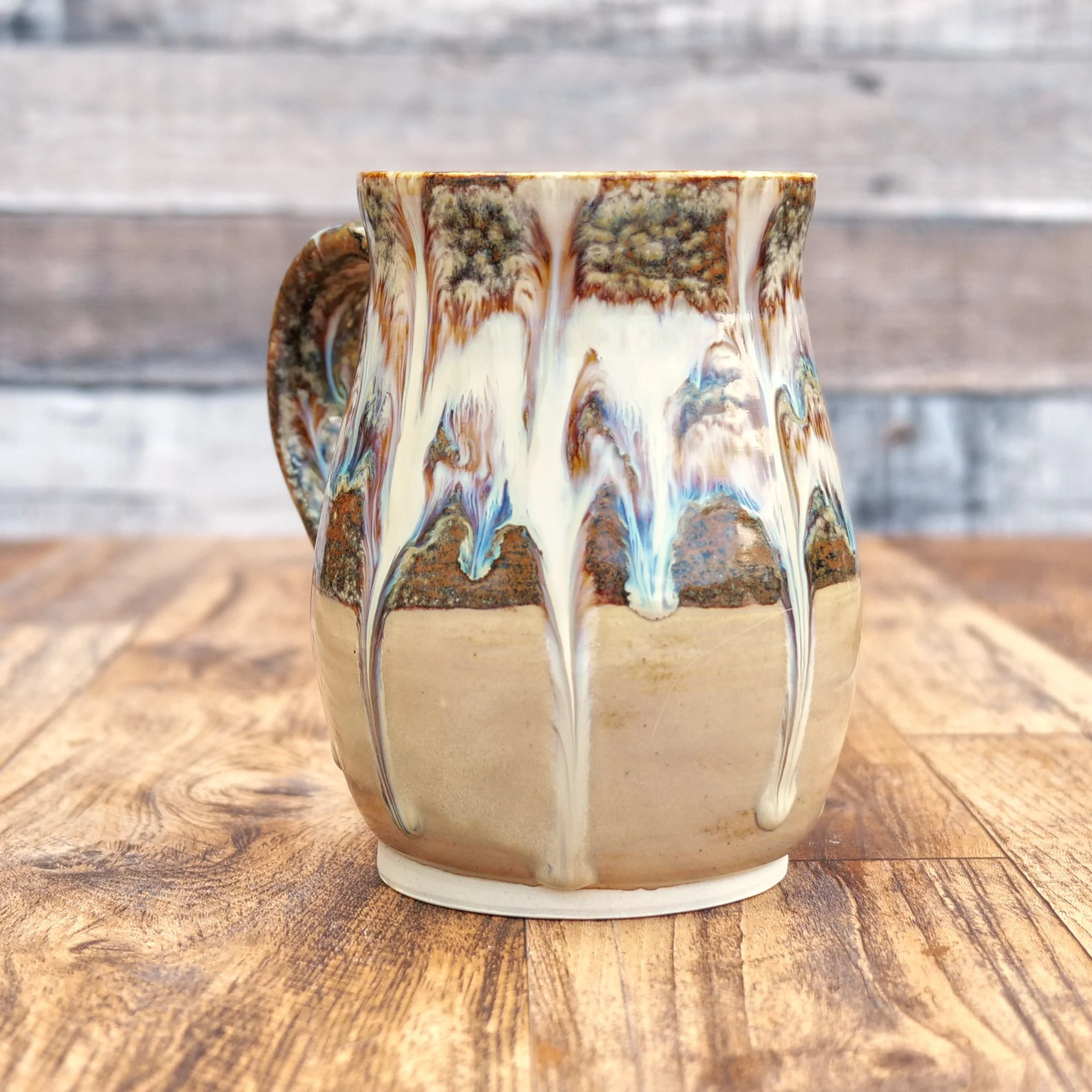Handmade stoneware Cascade Mug by Elderkiln Ceramics featuring flowing layered glazes in earthy brown, cream, and mineral tones on a rustic pottery mug.