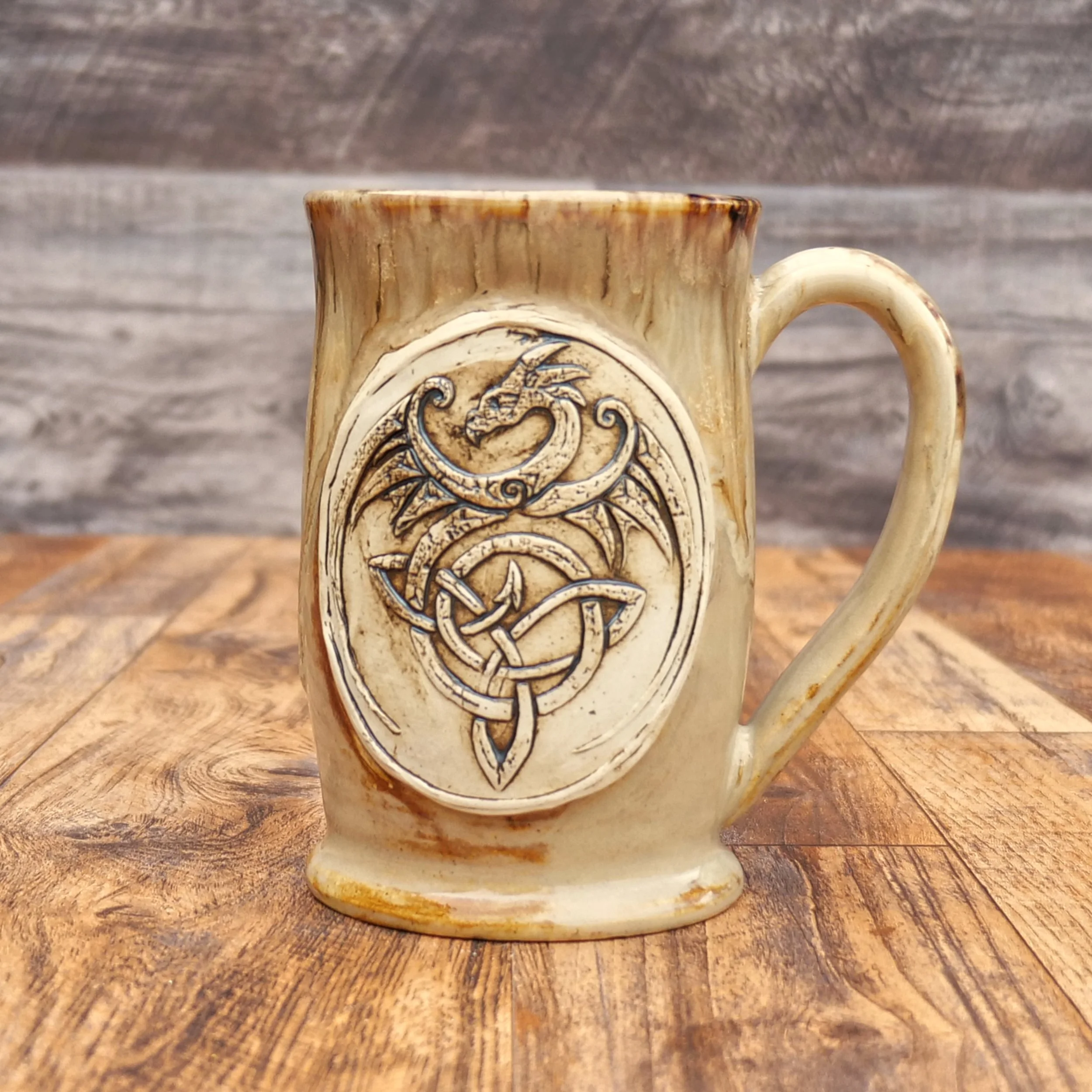 Handmade Celtic Dragon Mug by Elderkiln Ceramics featuring a sculpted dragon and Celtic knot design in warm earthy stoneware glazes.