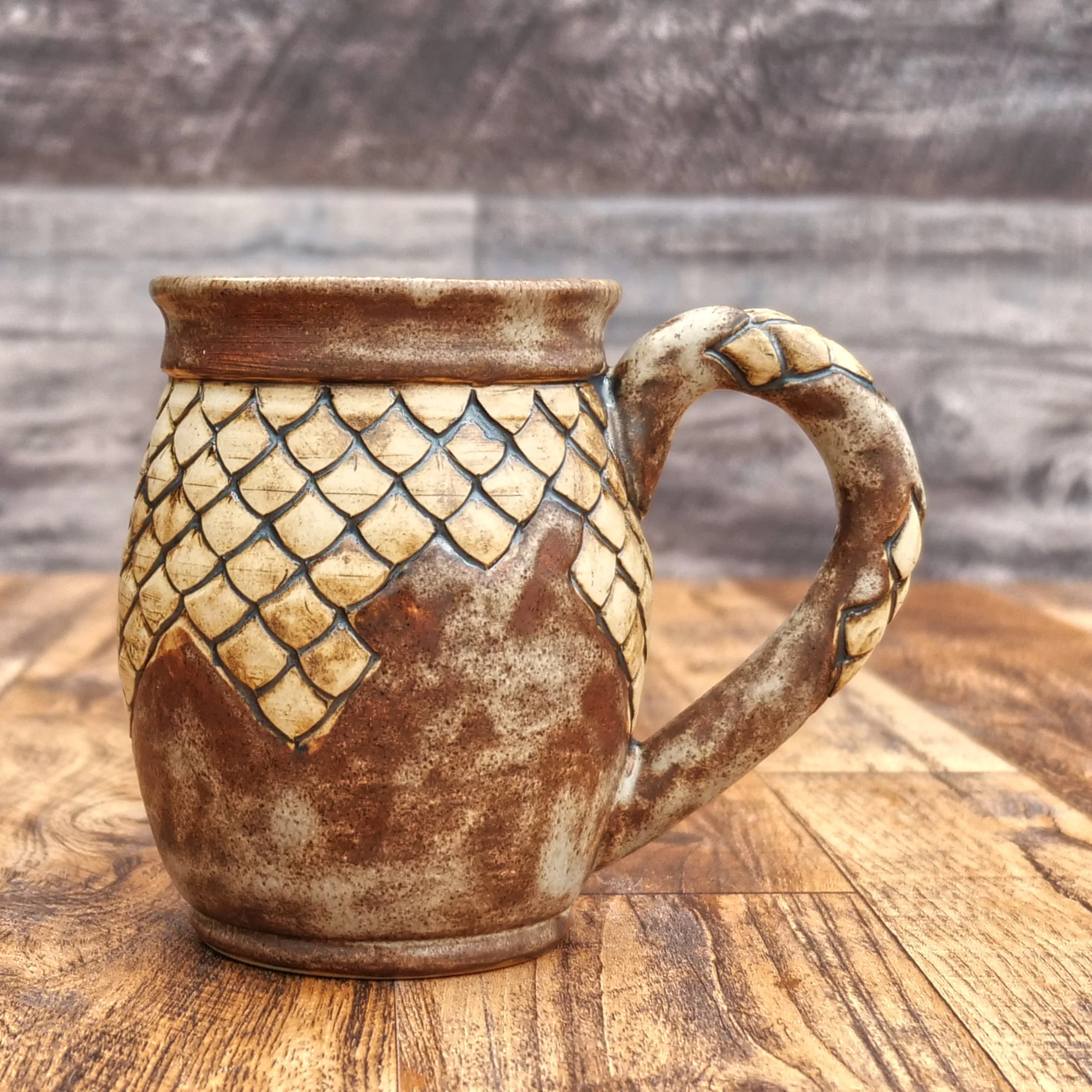 Handmade Dragonstone Mug by Elderkiln Ceramics featuring a sculpted dragon design, individually hand-carved scales, textured handle, and layered earthy brown stoneware glazes.