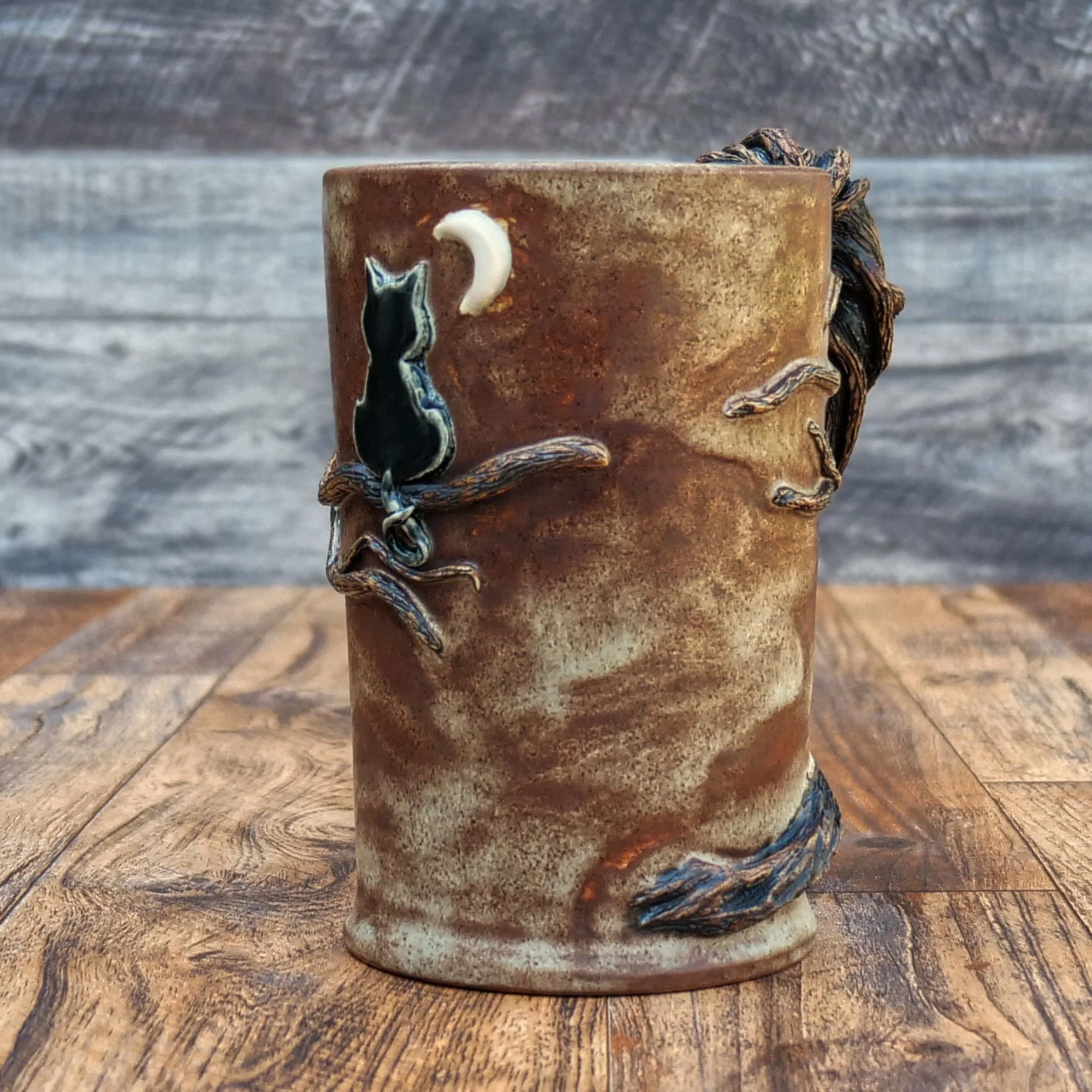 Handmade Moonwatcher Mug by Elderkiln Ceramics featuring a sculpted cat sitting on a tree branch beneath the moon, with wraparound woodland details and a twisted branch handle.